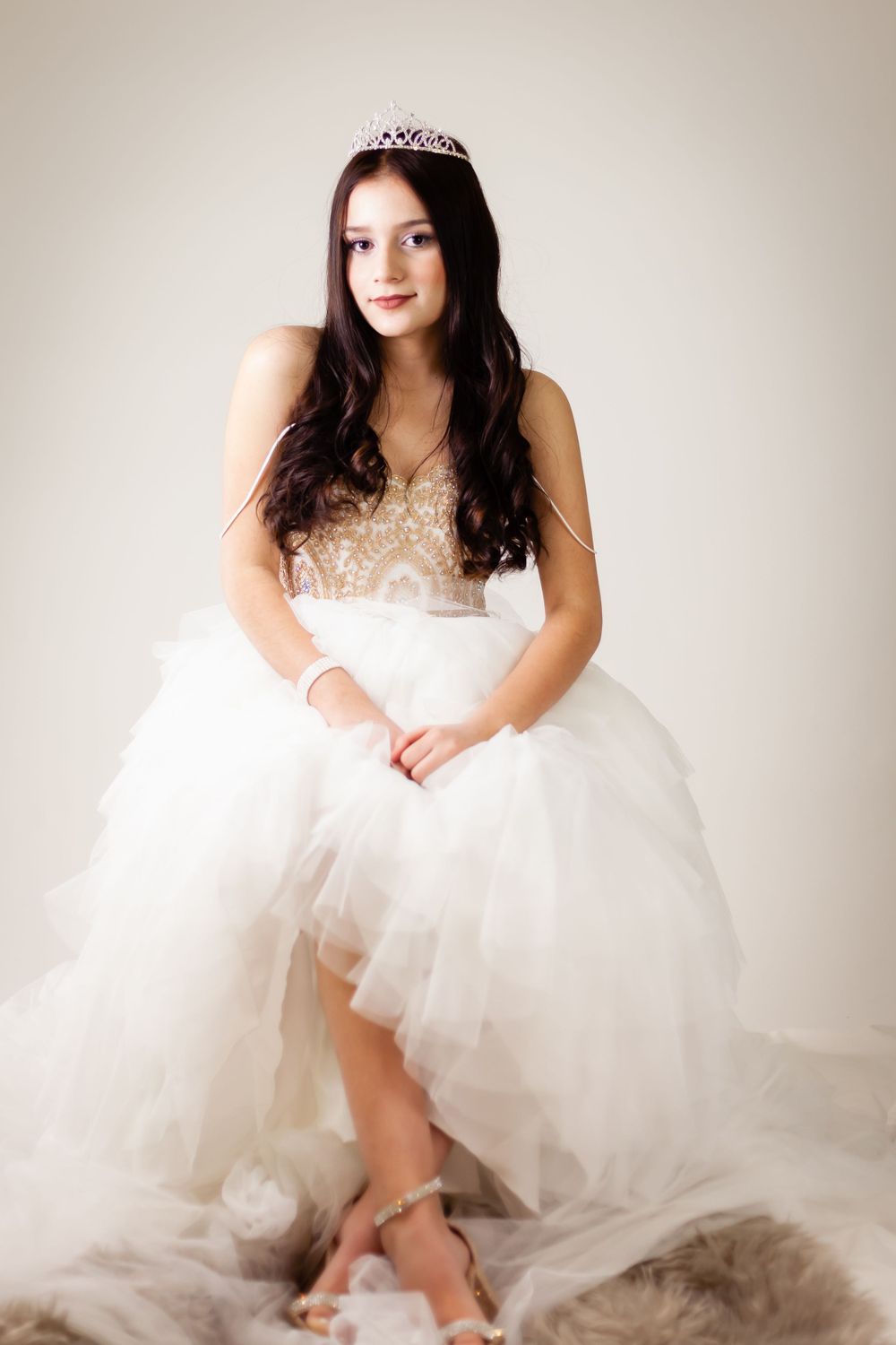 Ethereal portrait in a white tulle dress and sparkly tiara against beige background.