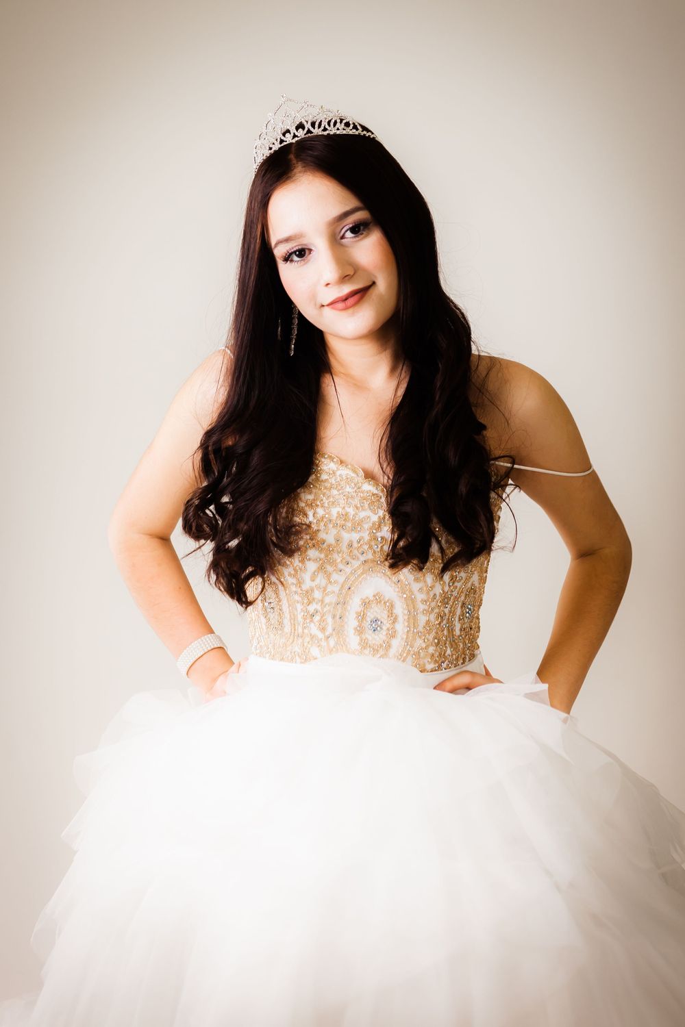 A portrait in a white ballgown with beaded bodice and tiara against neutral background.