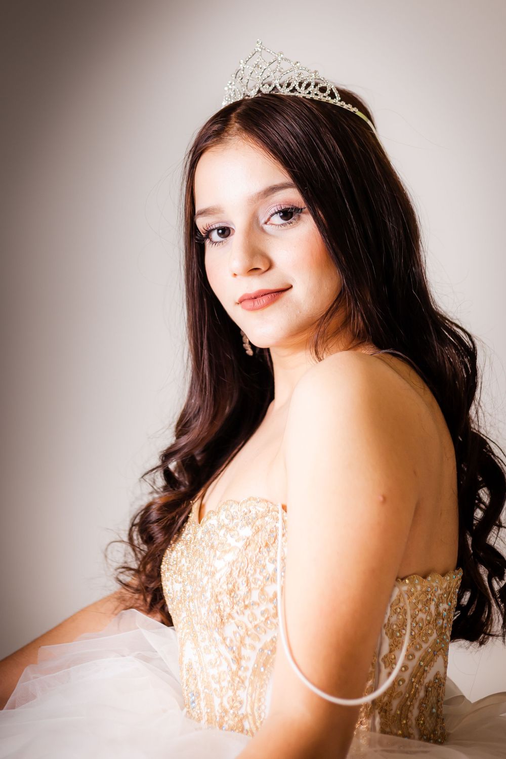 Classic portrait highlighting an embellished bodice gown and sparkling crown against neutral backdrop.