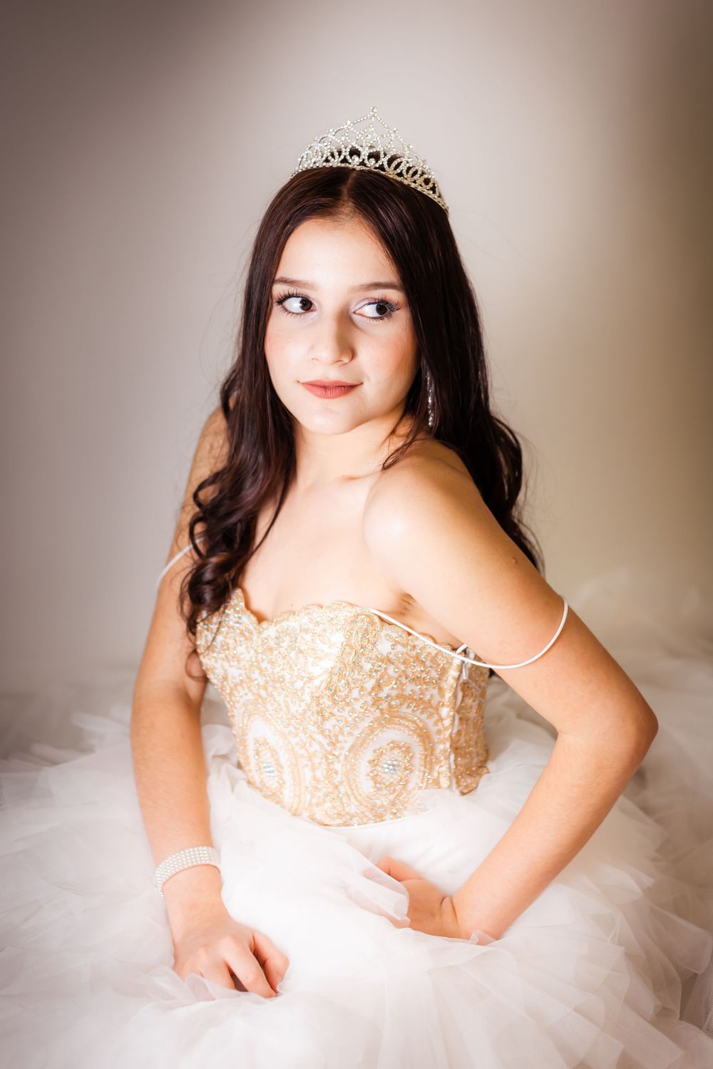 Graceful pose in an ornate gold and white ball gown with delicate crystal crown.
