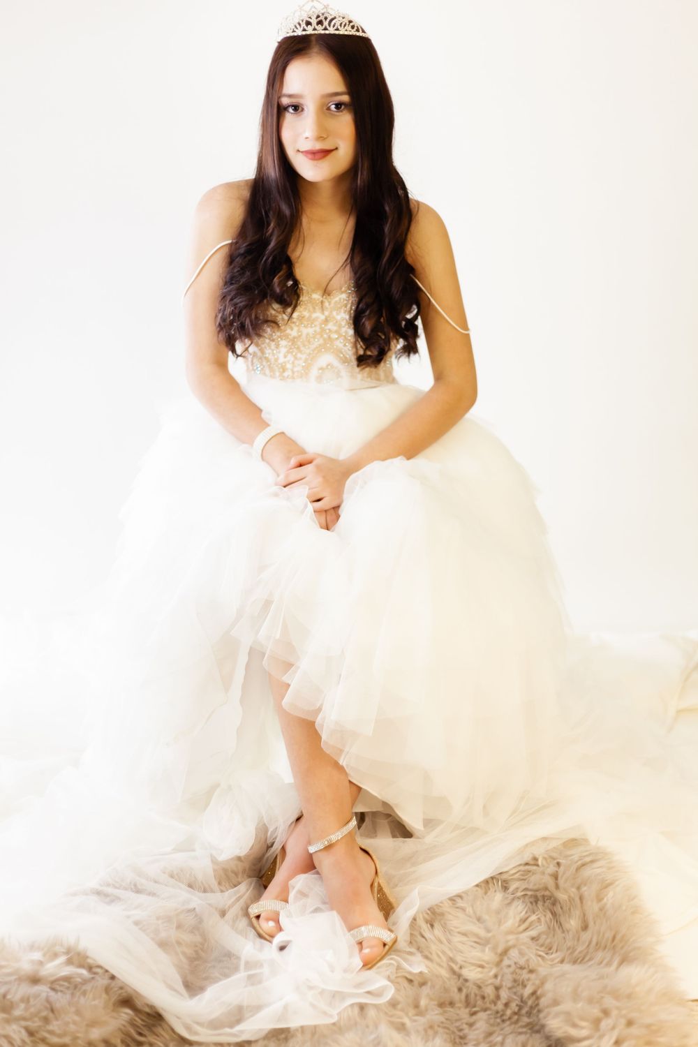 Elegant portrait in a white tulle gown and tiara against a neutral backdrop.