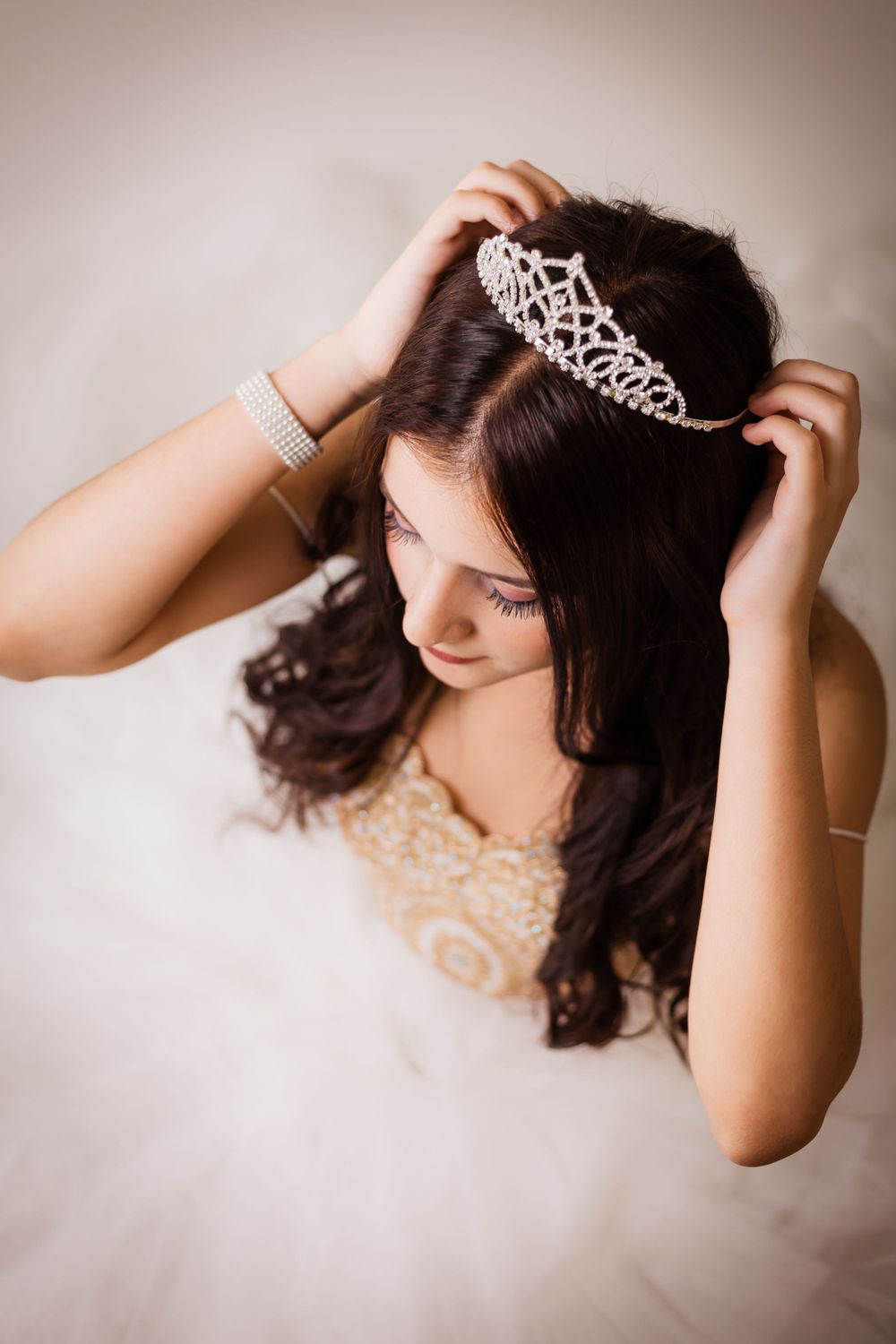 Someone adjusting a crystal tiara while wearing an ornate beige gown.