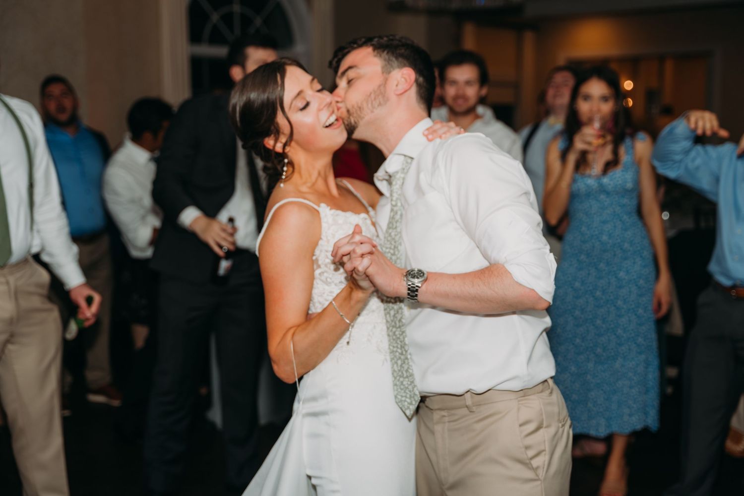 Wedding guests dance and celebrate on a dimly lit dance floor at an evening reception.