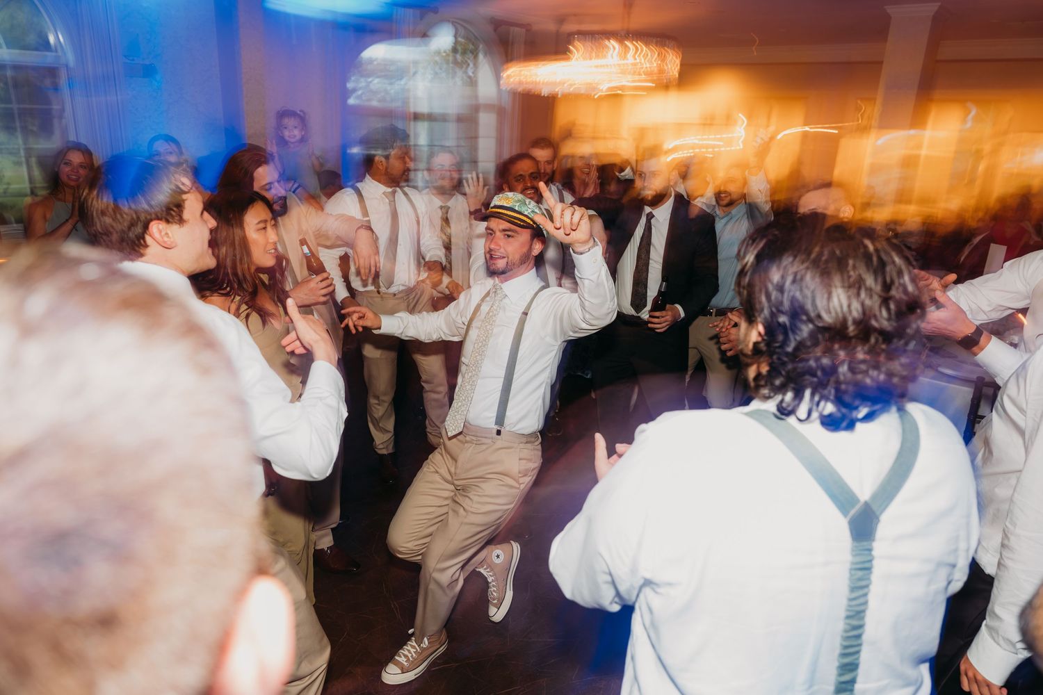 Wedding guests dancing energetically on a dance floor with blue lighting.
