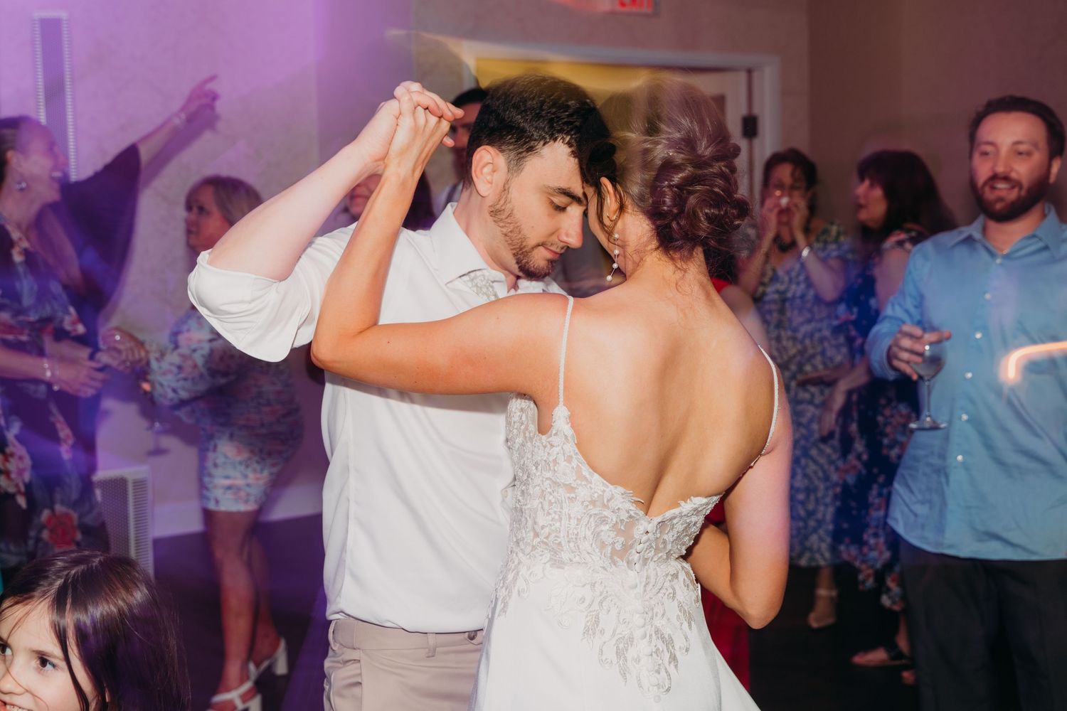 Couples dancing together during a lively wedding reception with purple ambient lighting.