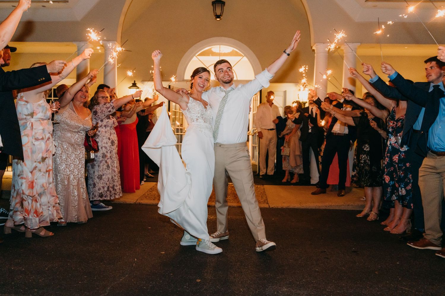 Wedding party dances under string lights in an elegant indoor venue.