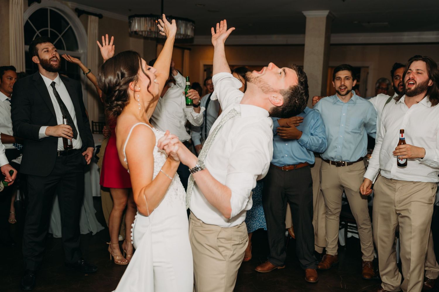 Wedding guests dancing and celebrating with raised arms in an elegant venue.