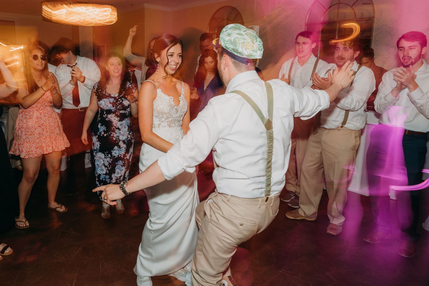 Wedding reception dance floor filled with guests celebrating under pink and purple lighting.