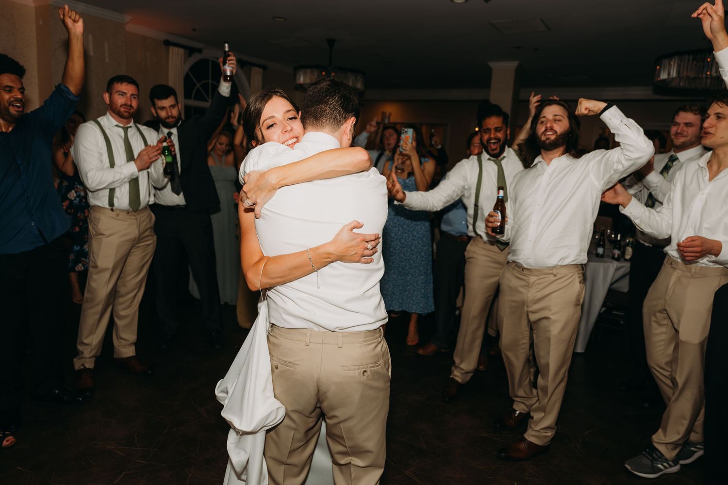 Guests in formal attire dance energetically at a wedding reception in a dark venue.