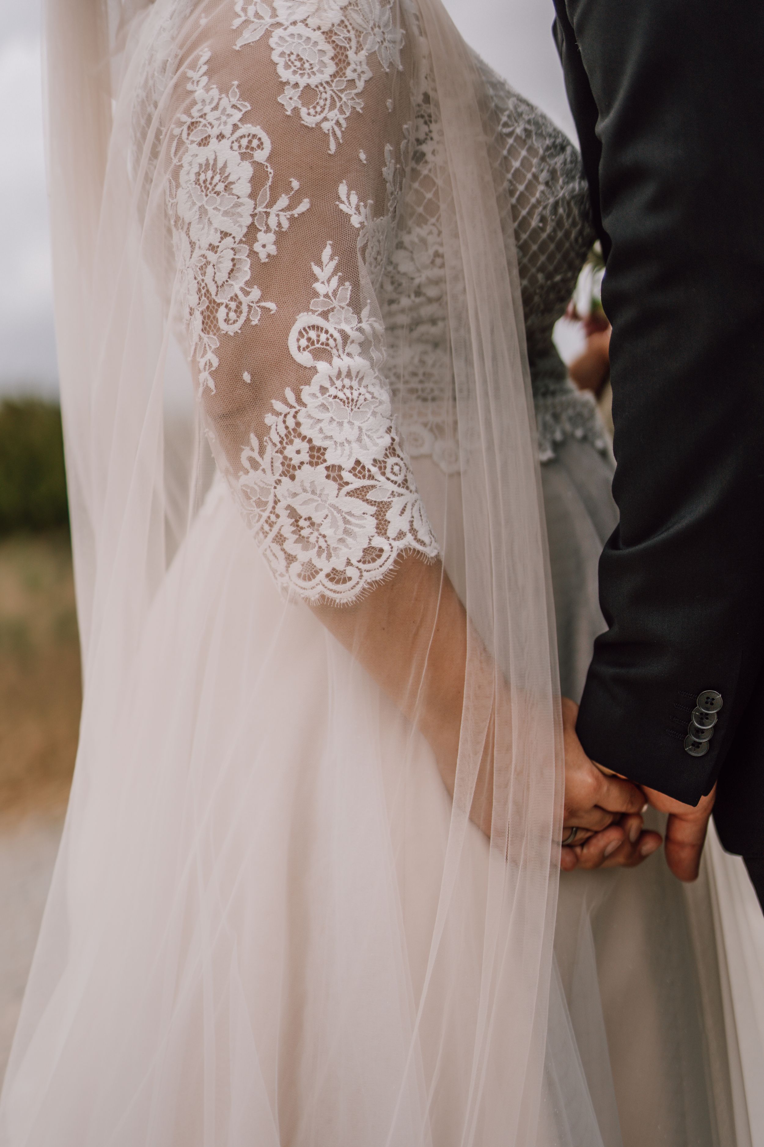 Detail shot of delicate lace sleeve wedding dress and black tuxedo.