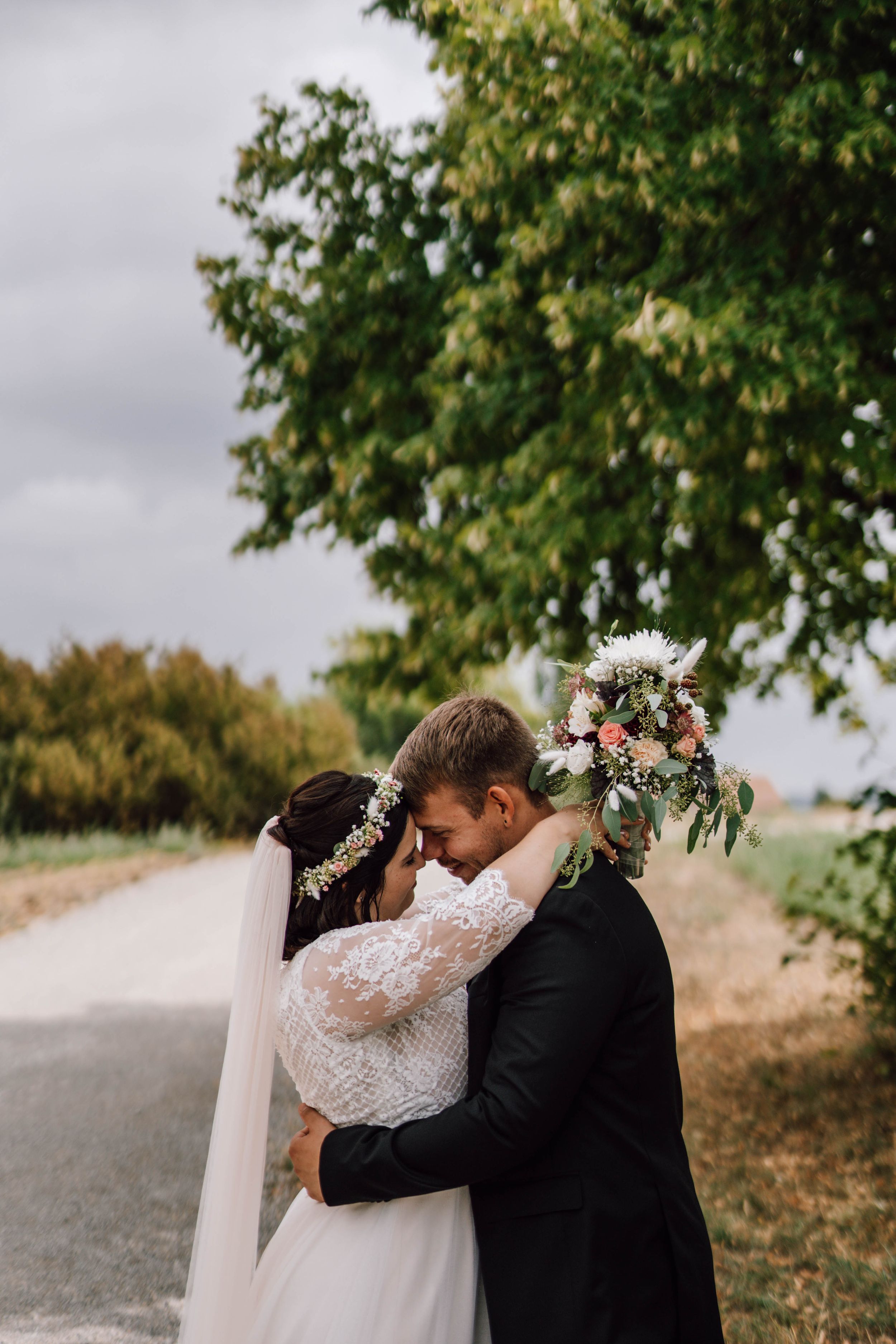 Intimate wedding moment captured under a tree on a rural path.