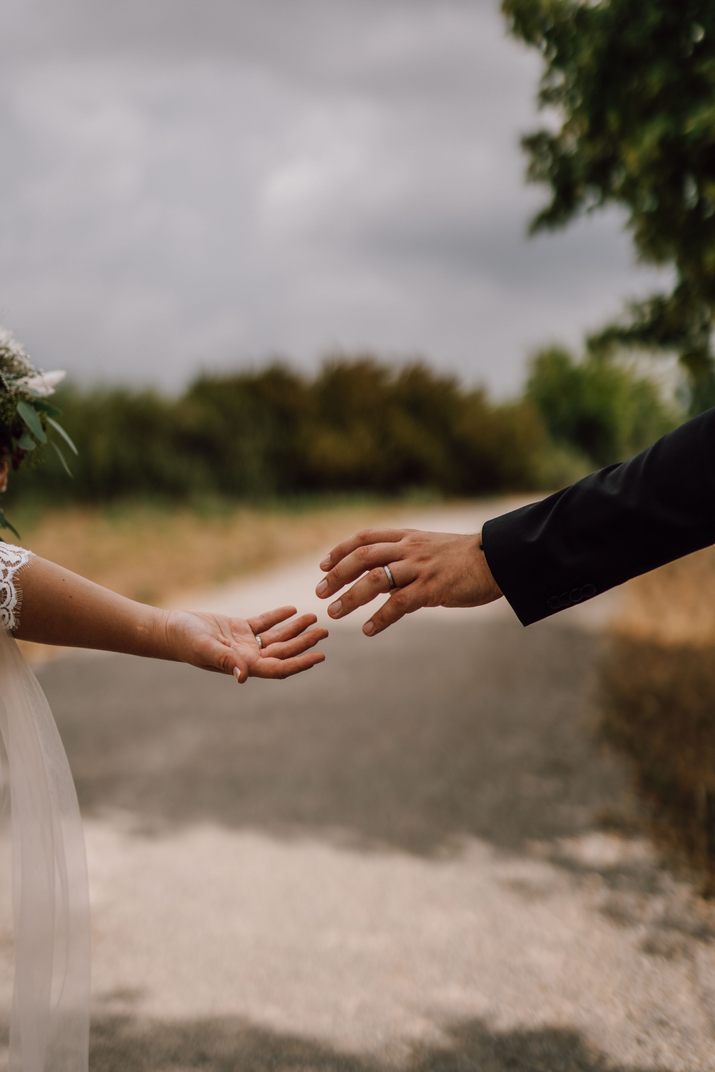 Artistic shot of bride and groom reaching for each other's hands on country road.