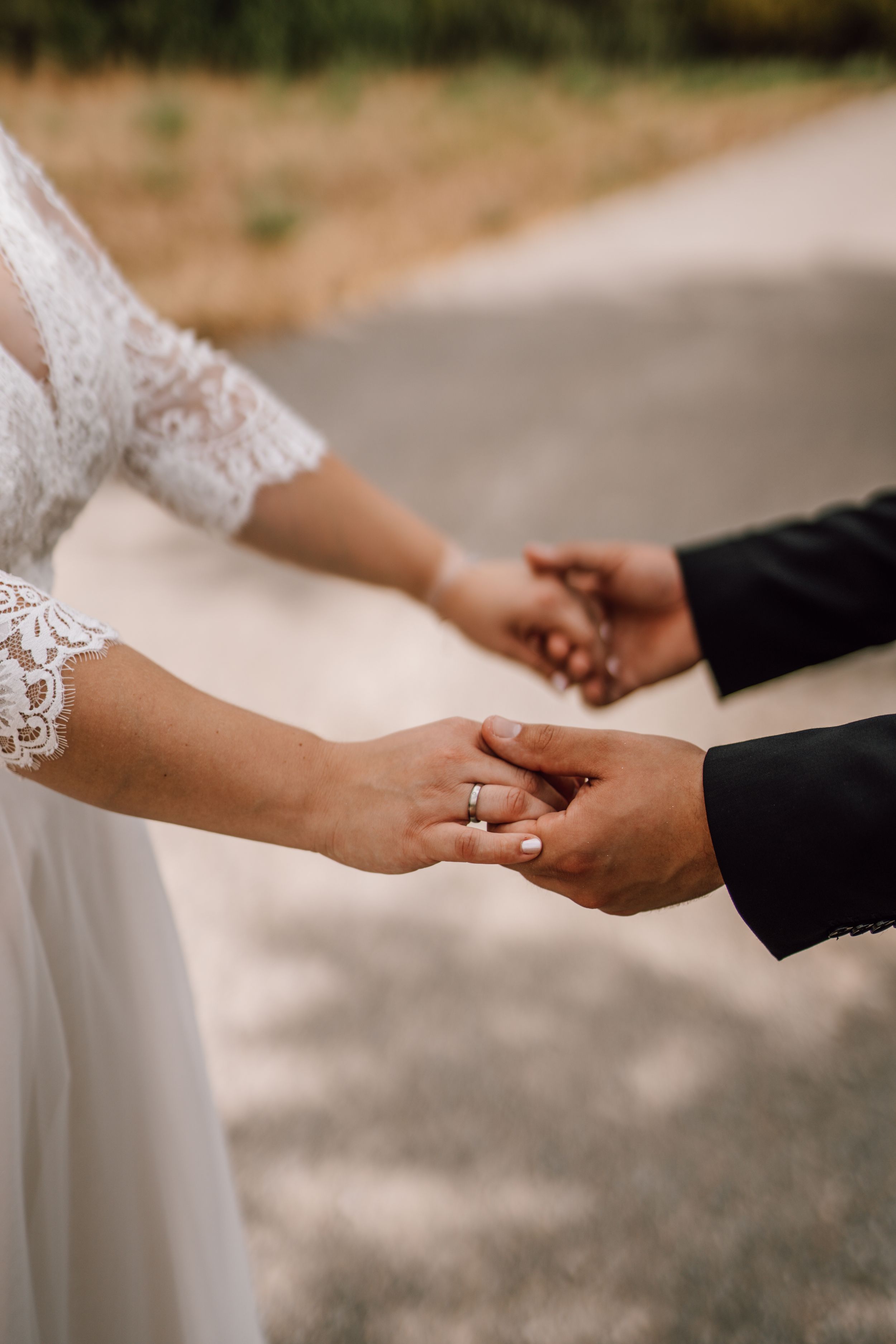 Close-up of bride and groom holding hands showing wedding rings and lace sleeves.