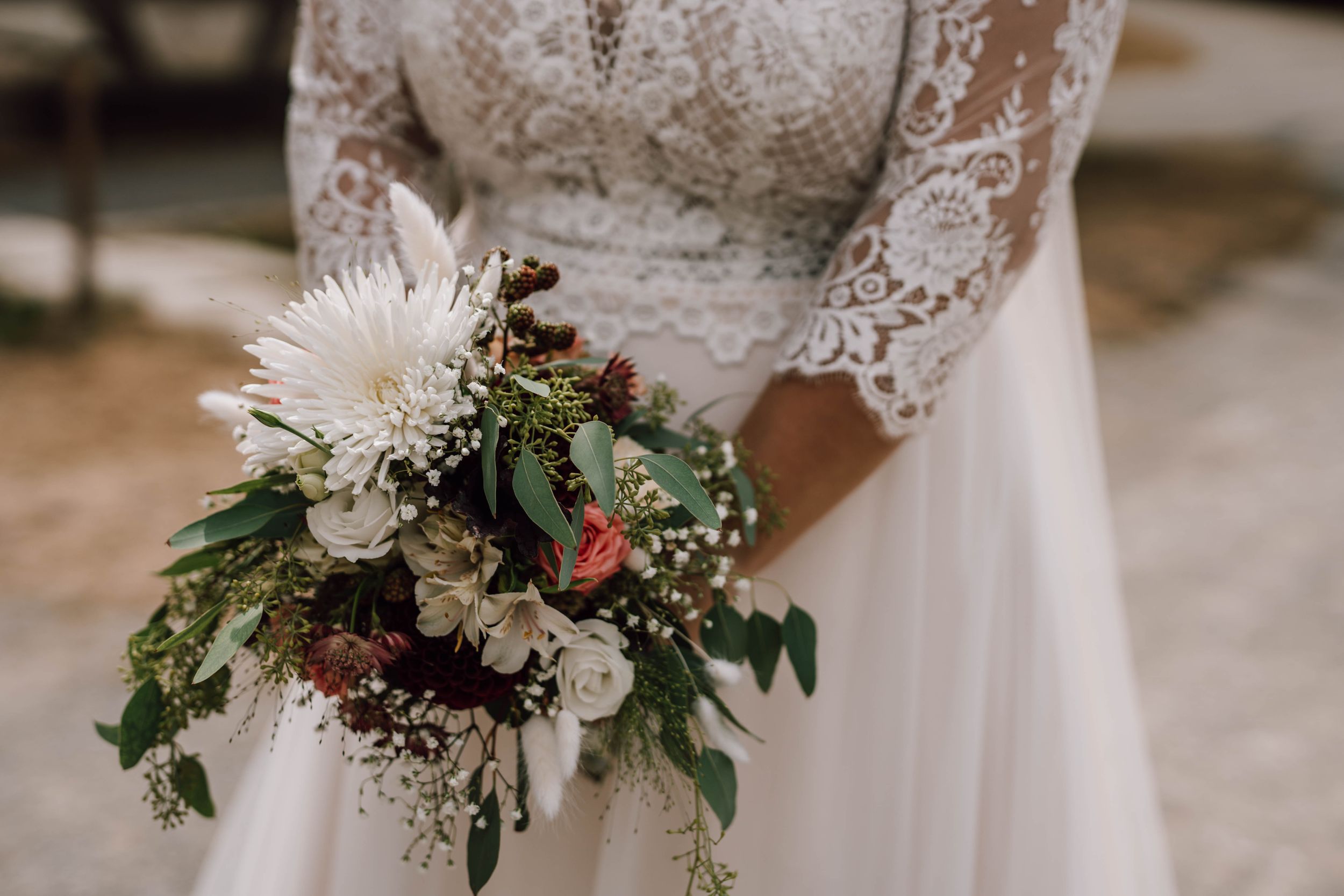 Elegant wedding bouquet features fresh flowers and greenery against white dress.