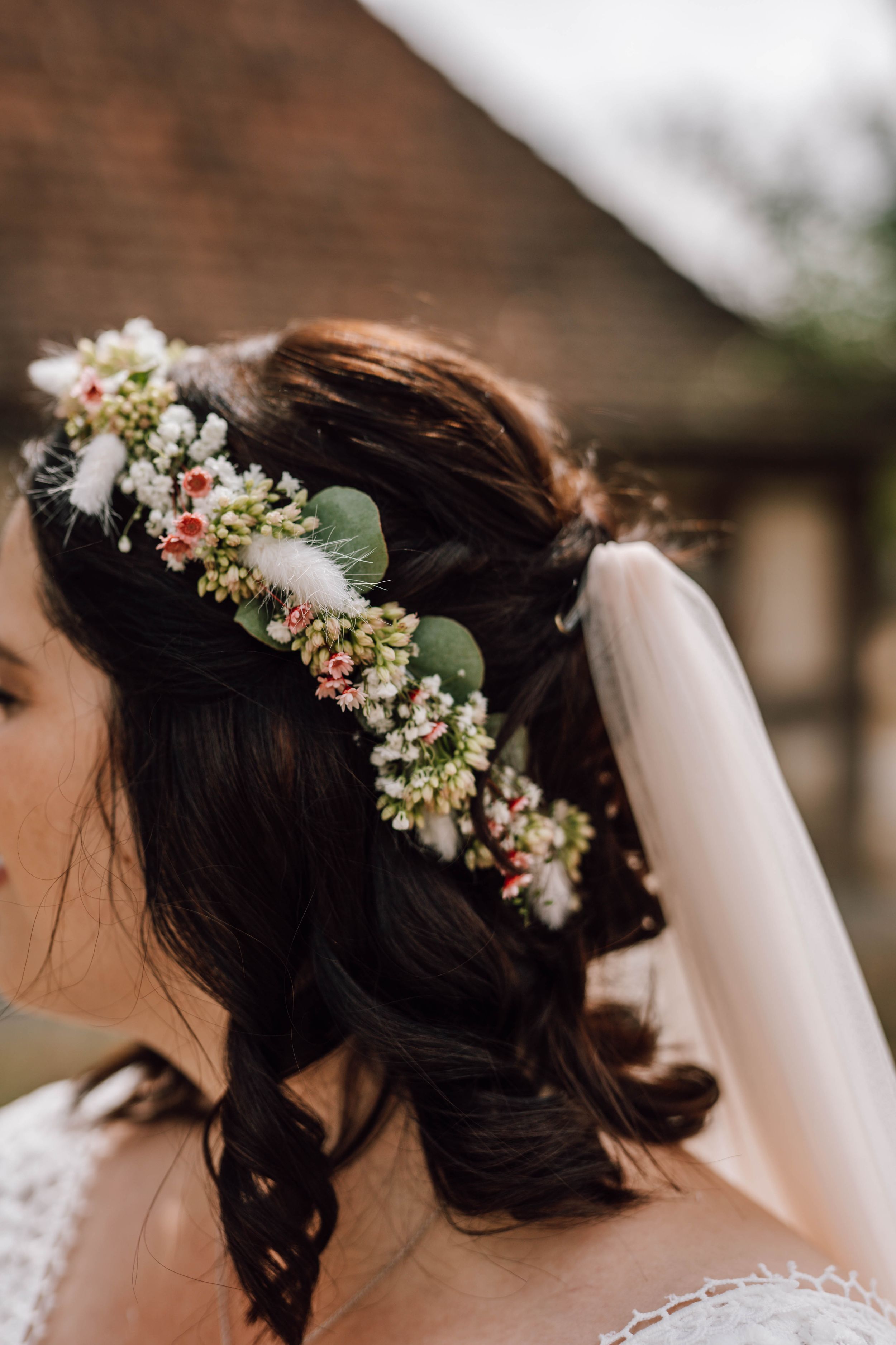 Delicate floral crown adorns bride's dark hair with white veil attachment.