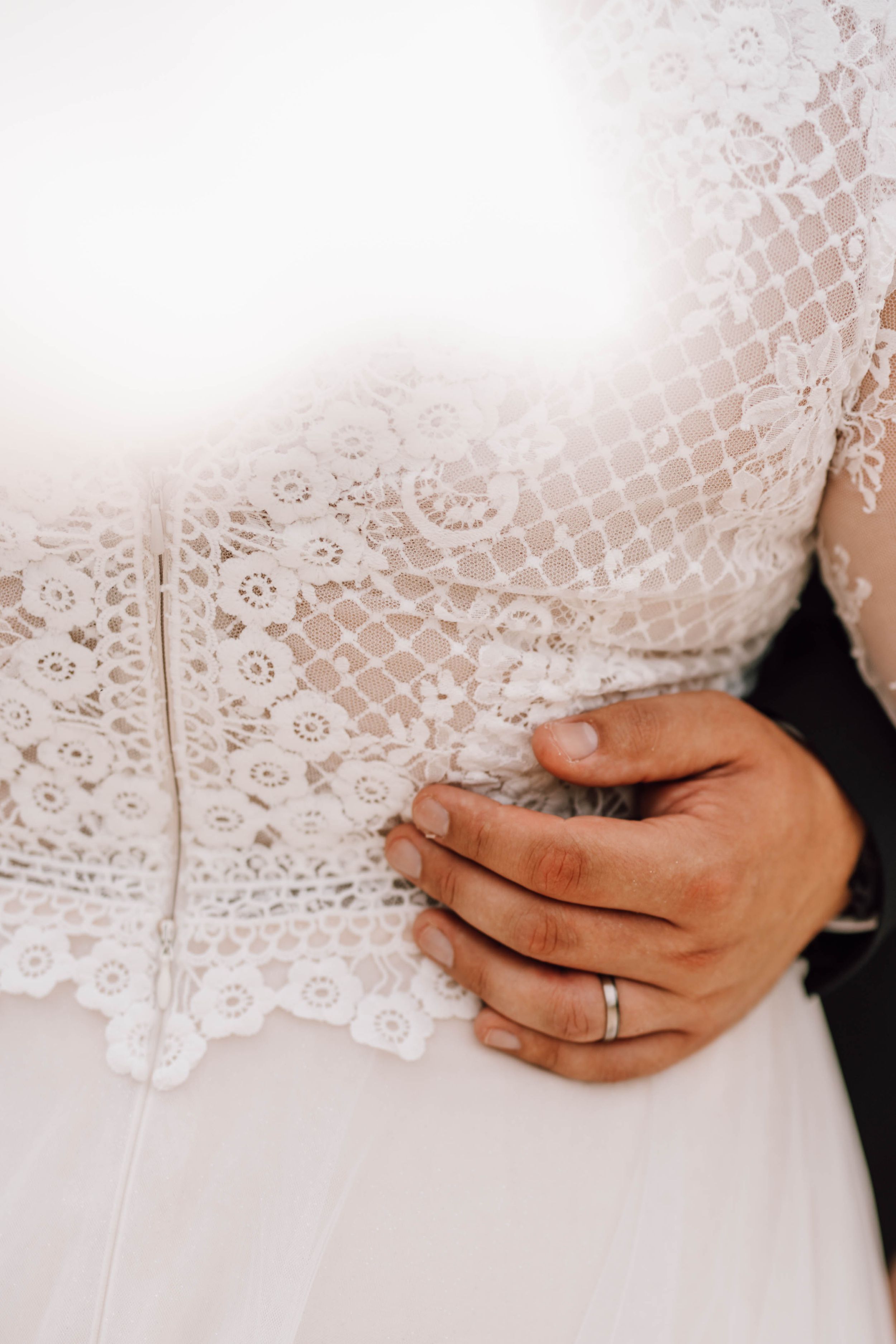 Close-up detail of intricate lace wedding dress pattern and wedding ring.