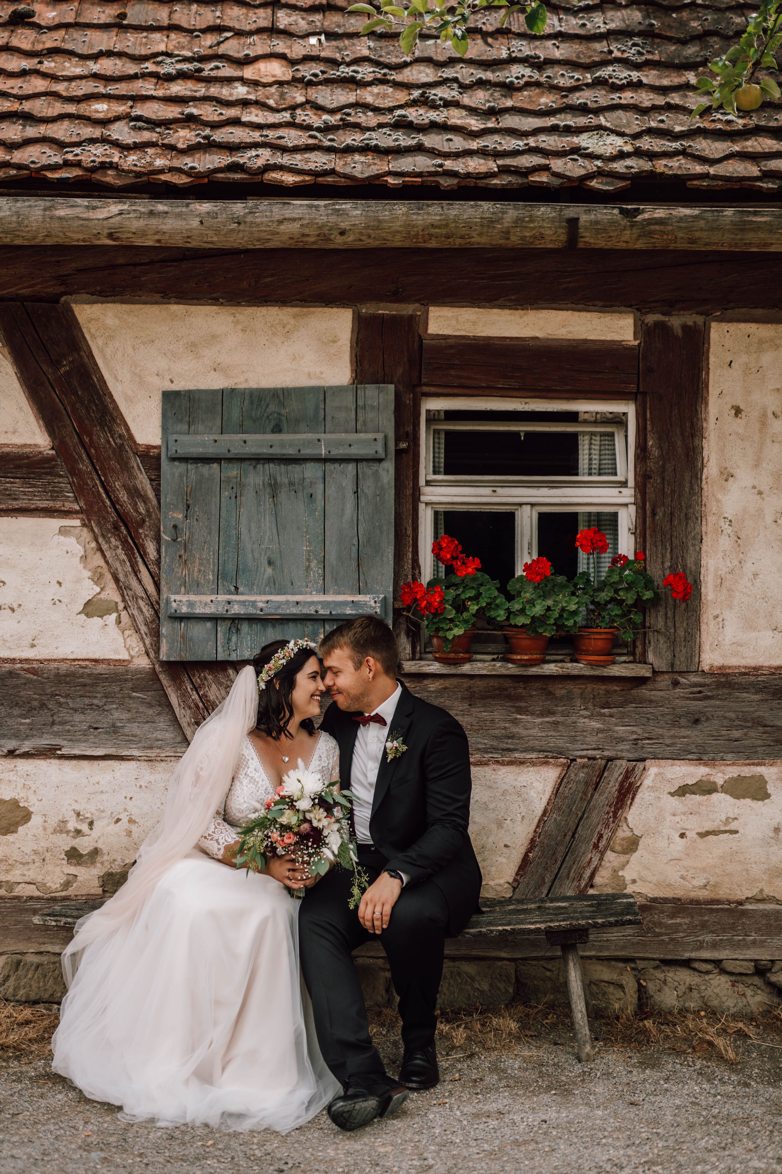 Rustic farmhouse setting with red window flowers frames wedding couple.