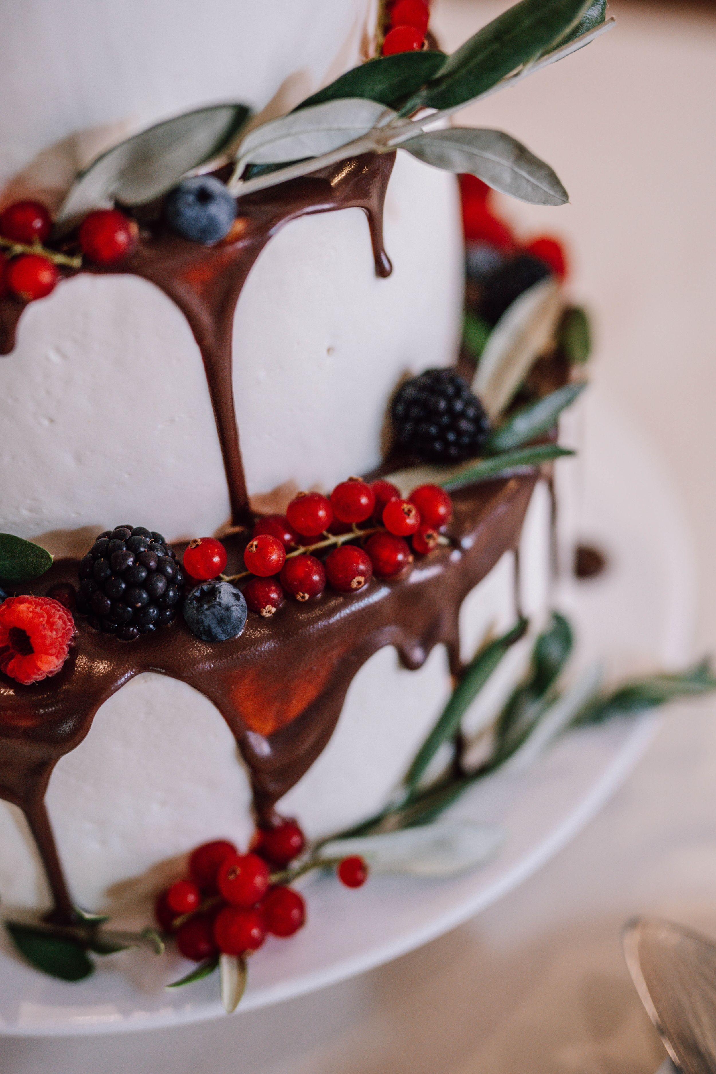 Wedding cake decorated with chocolate drip and fresh berries on white plate.