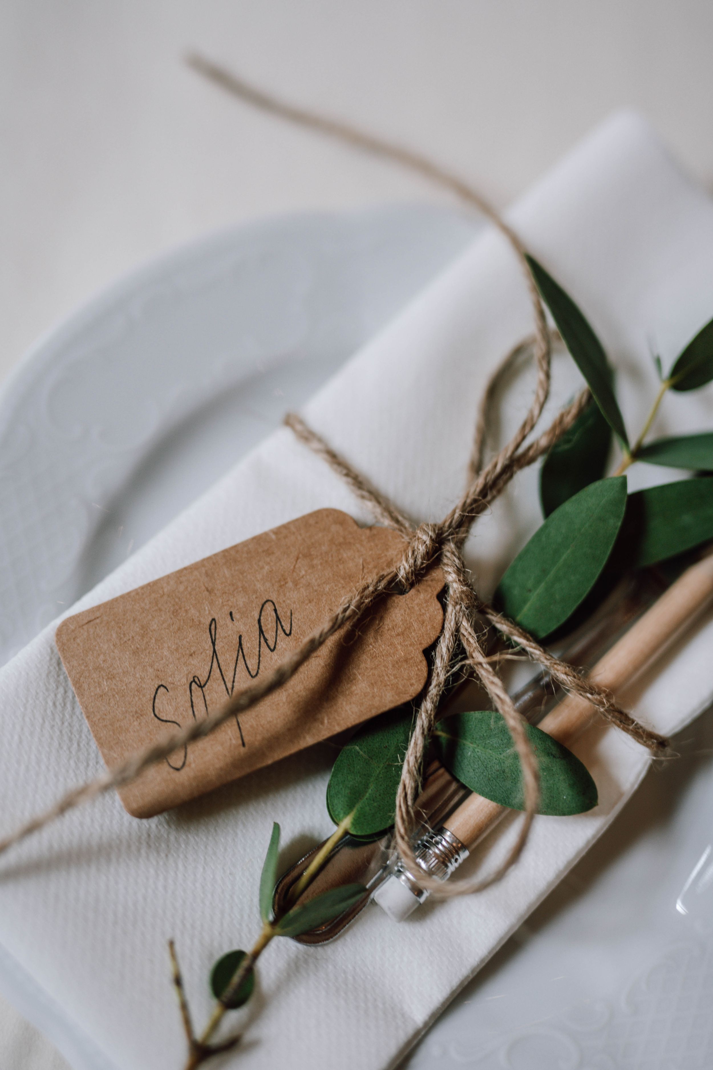 Place setting with kraft paper name tag, twine, and eucalyptus sprig on white plate.