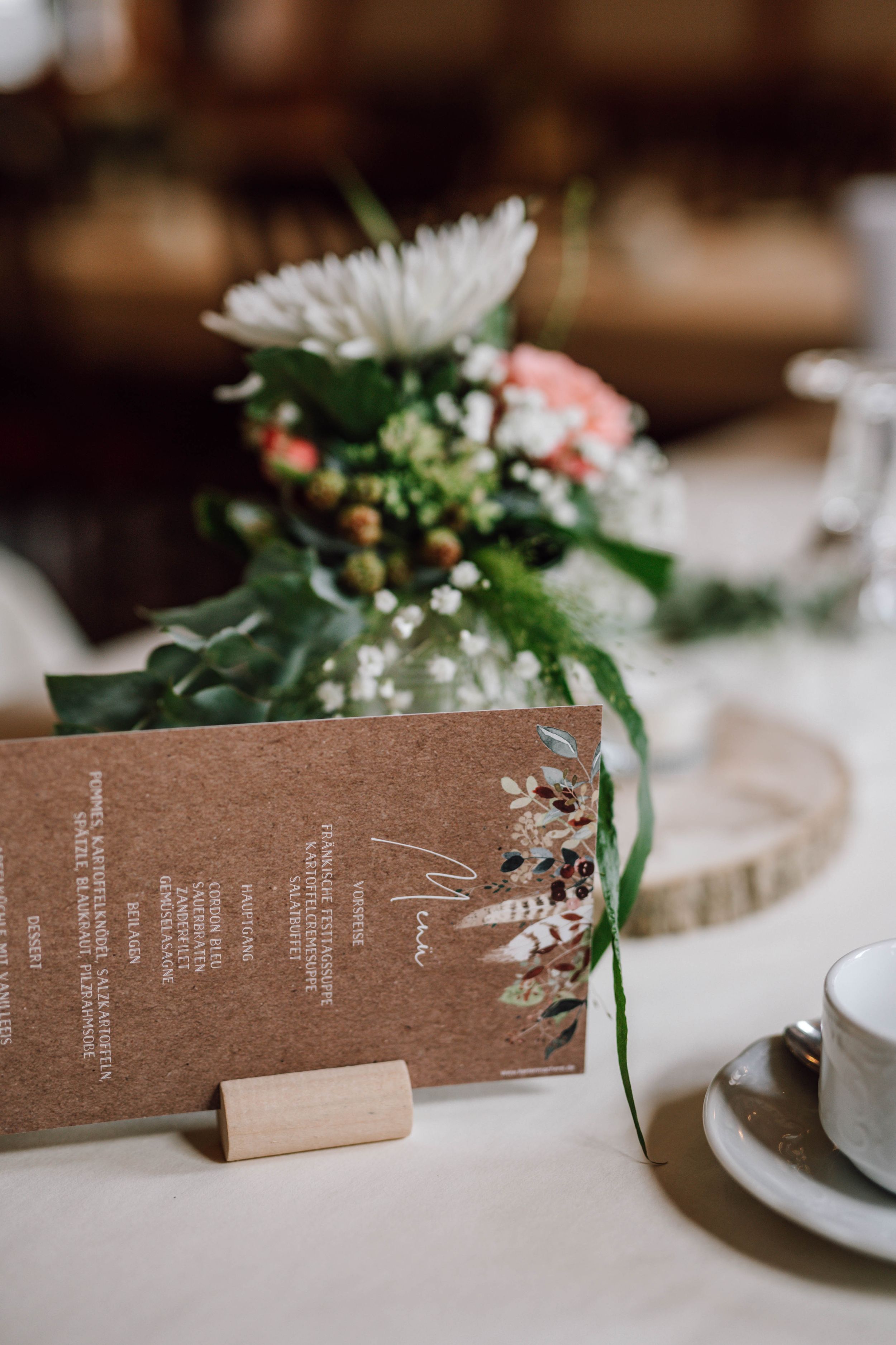 Wedding menu card and floral centerpiece on rustic wood slice with teacup.