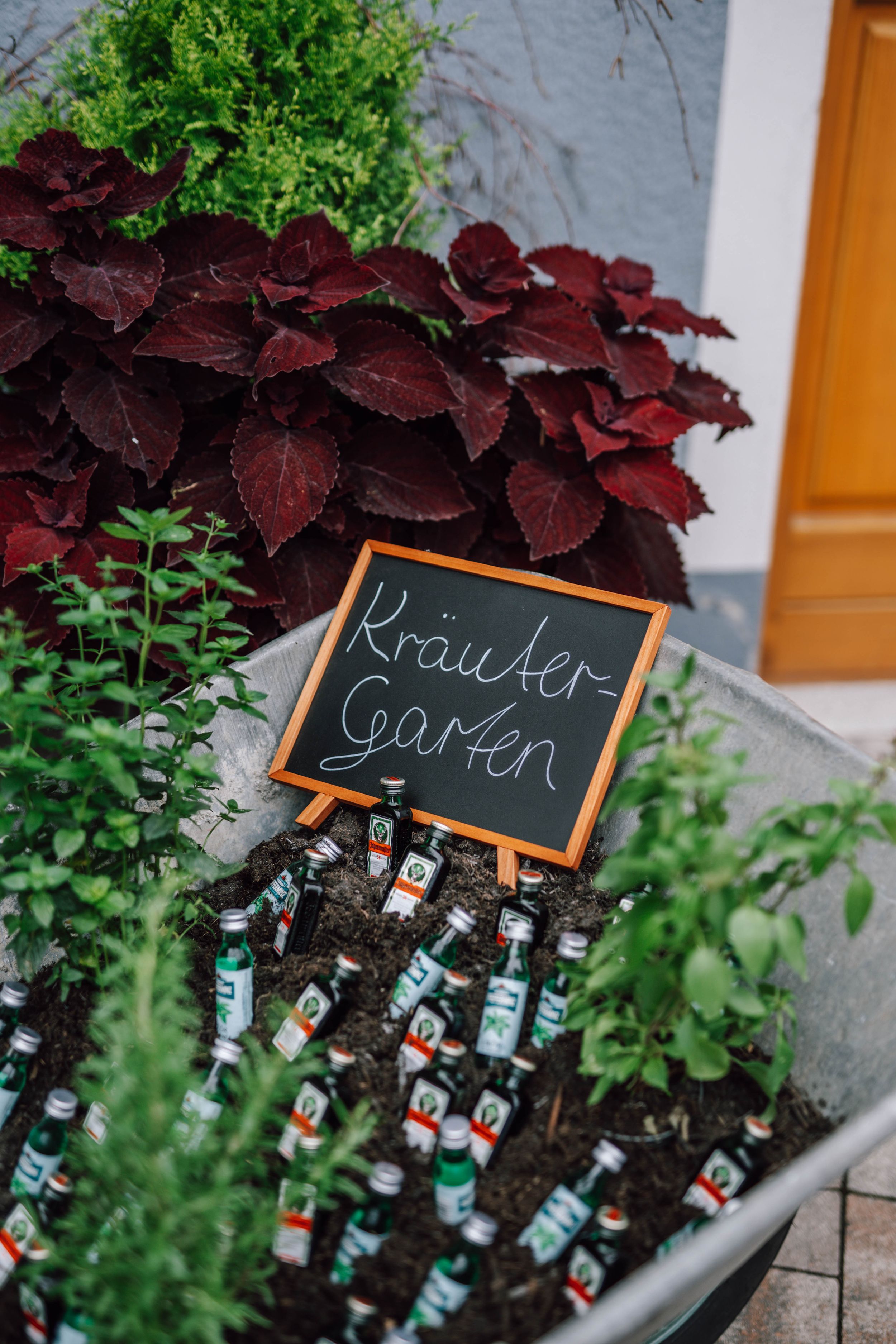 Herb garden sign with red coleus plants and bottles arranged in outdoor planter.