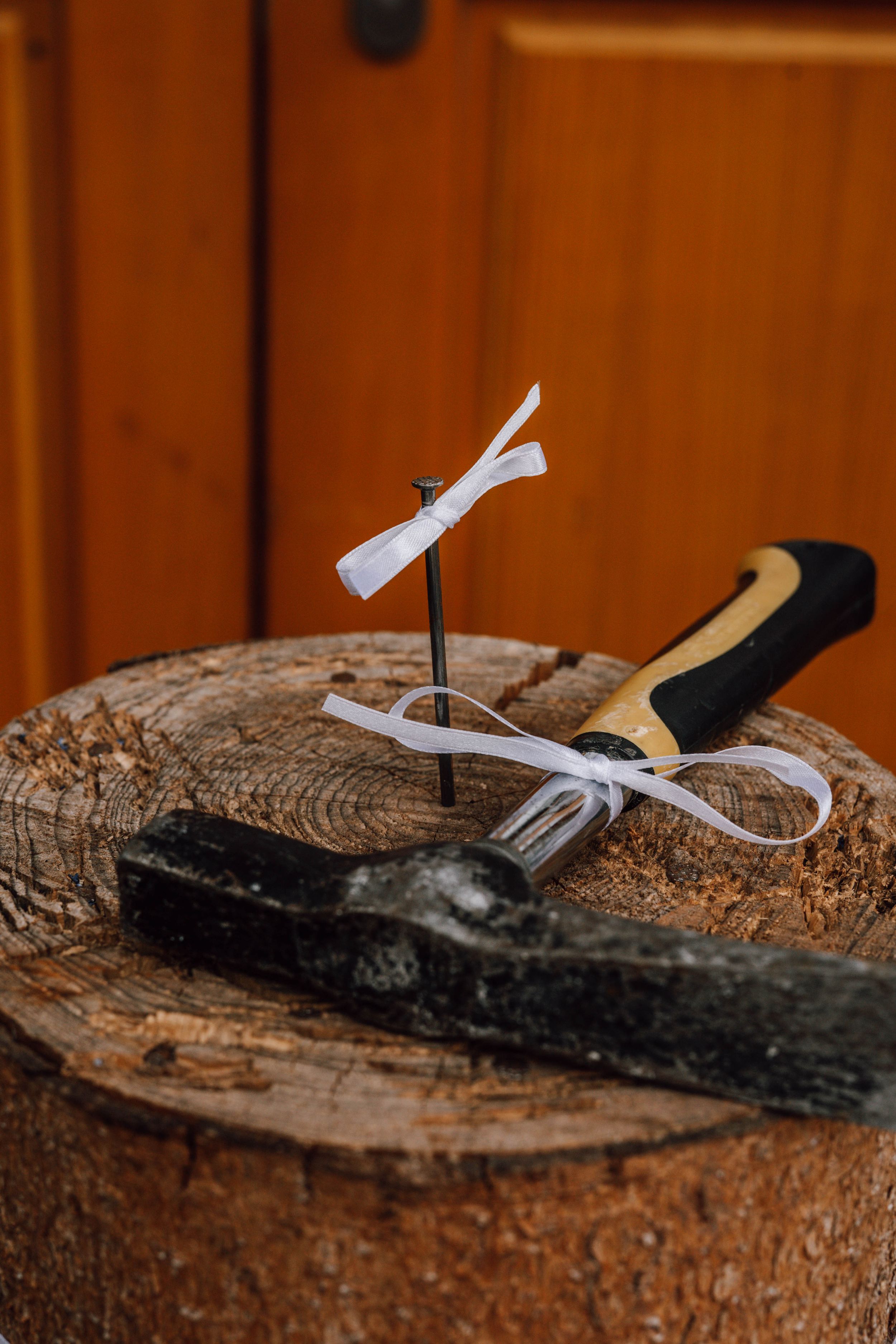 Rolled white paper tied with ribbon on rustic wood slice with hammer.