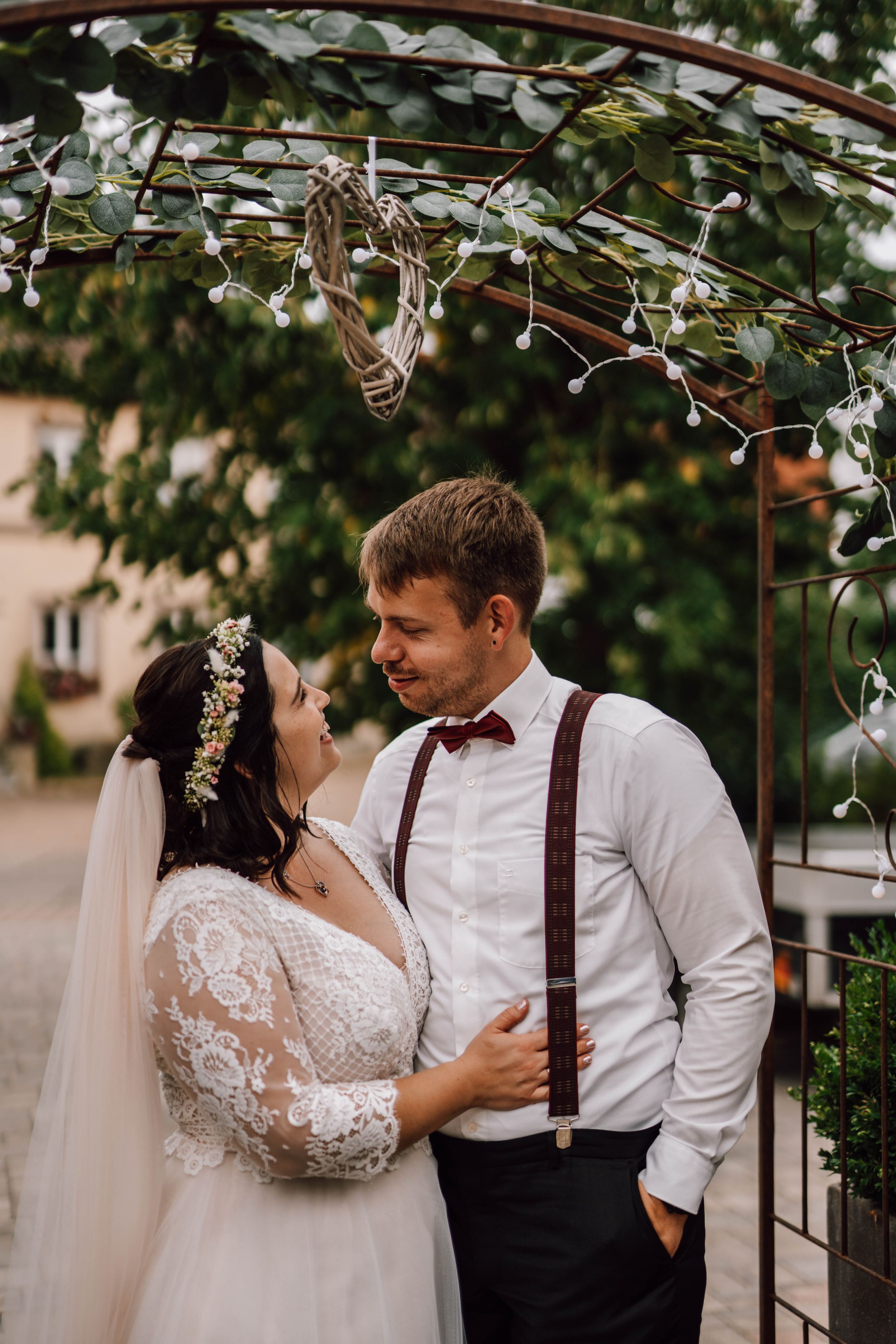 A romantic wedding couple shares intimate moments under a floral arch in an outdoor garden setting.