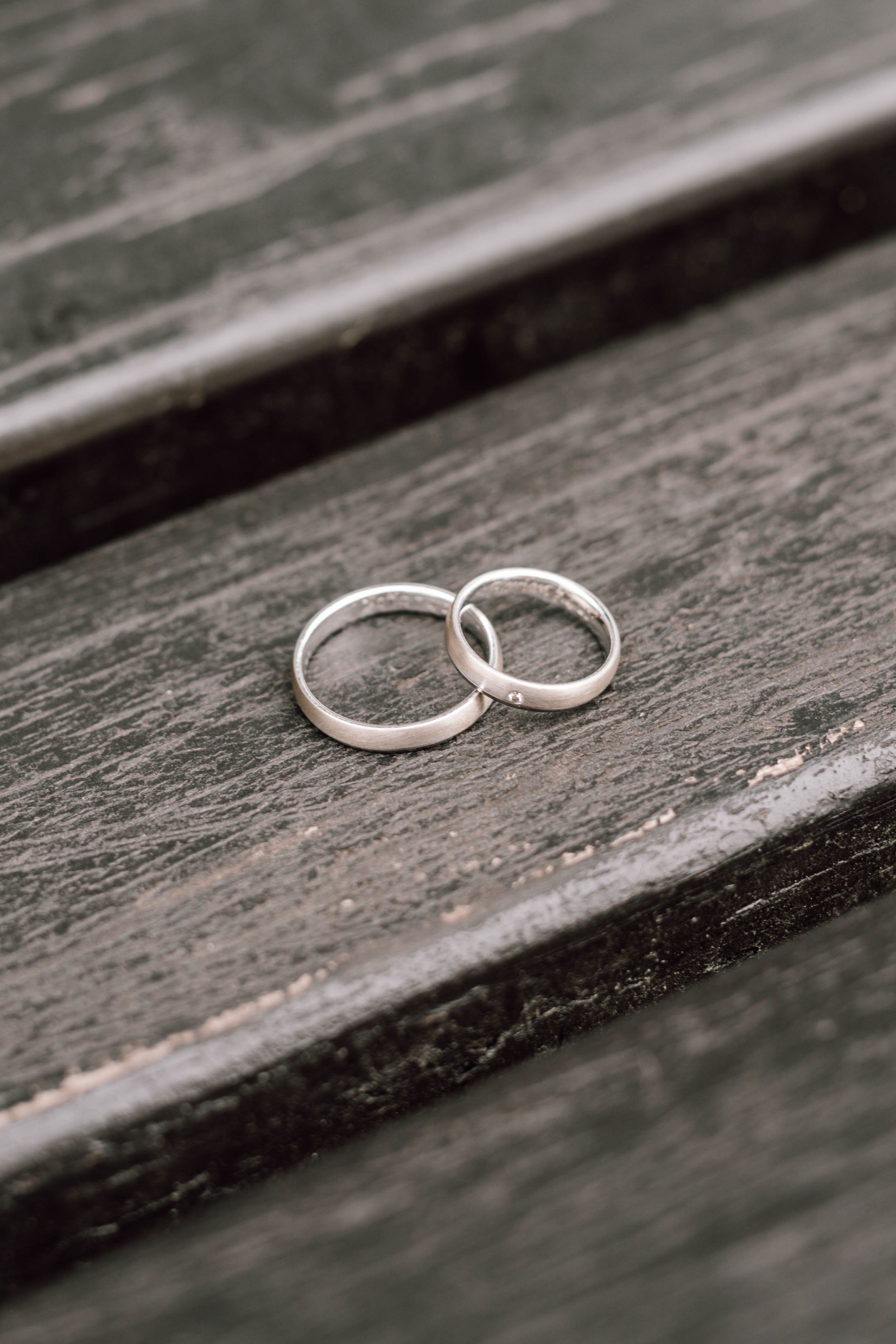 Two silver wedding rings rest on a weathered wooden surface in black and white.