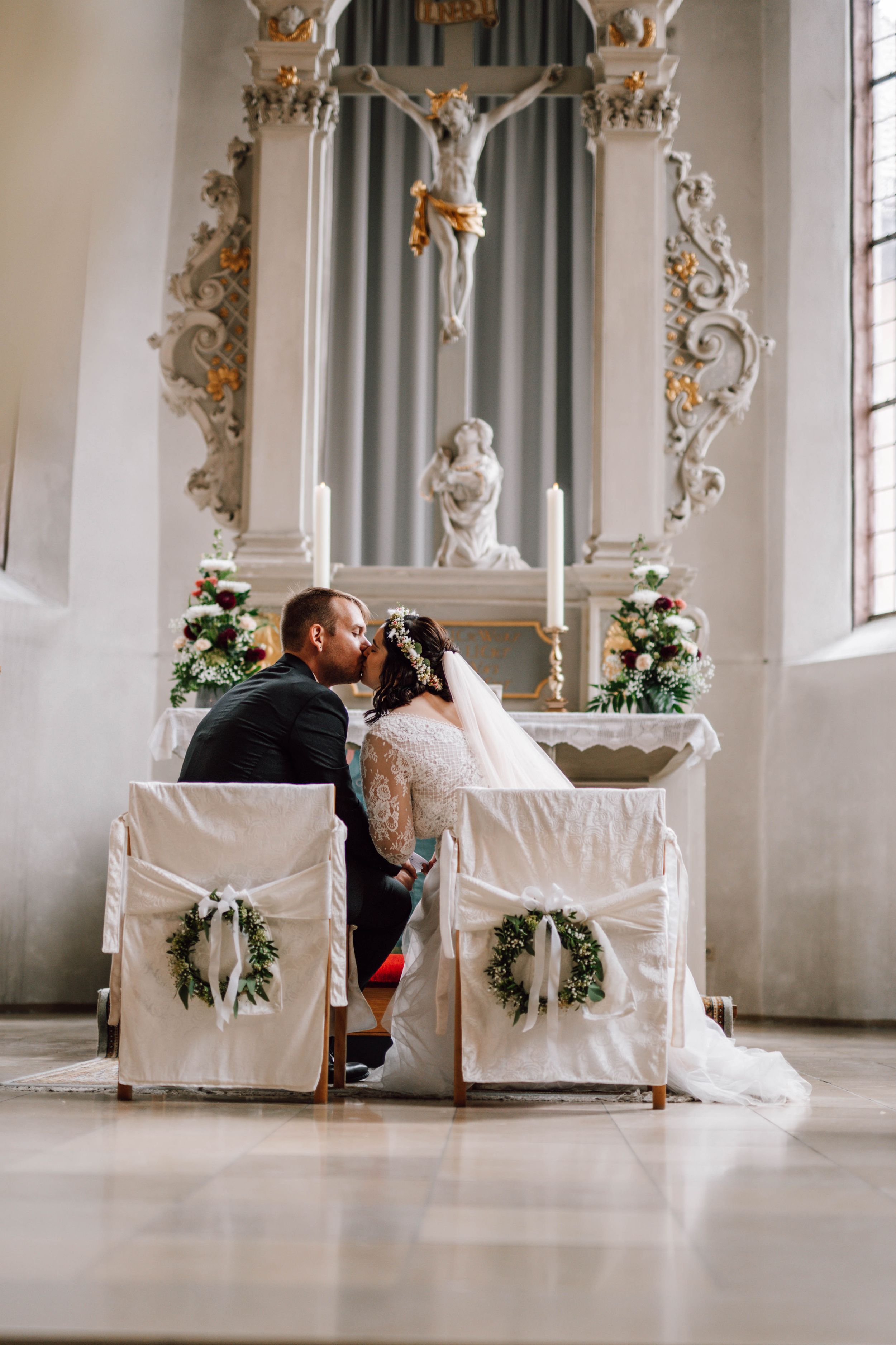 Newlyweds share an intimate moment in an ornate white church with baroque details.