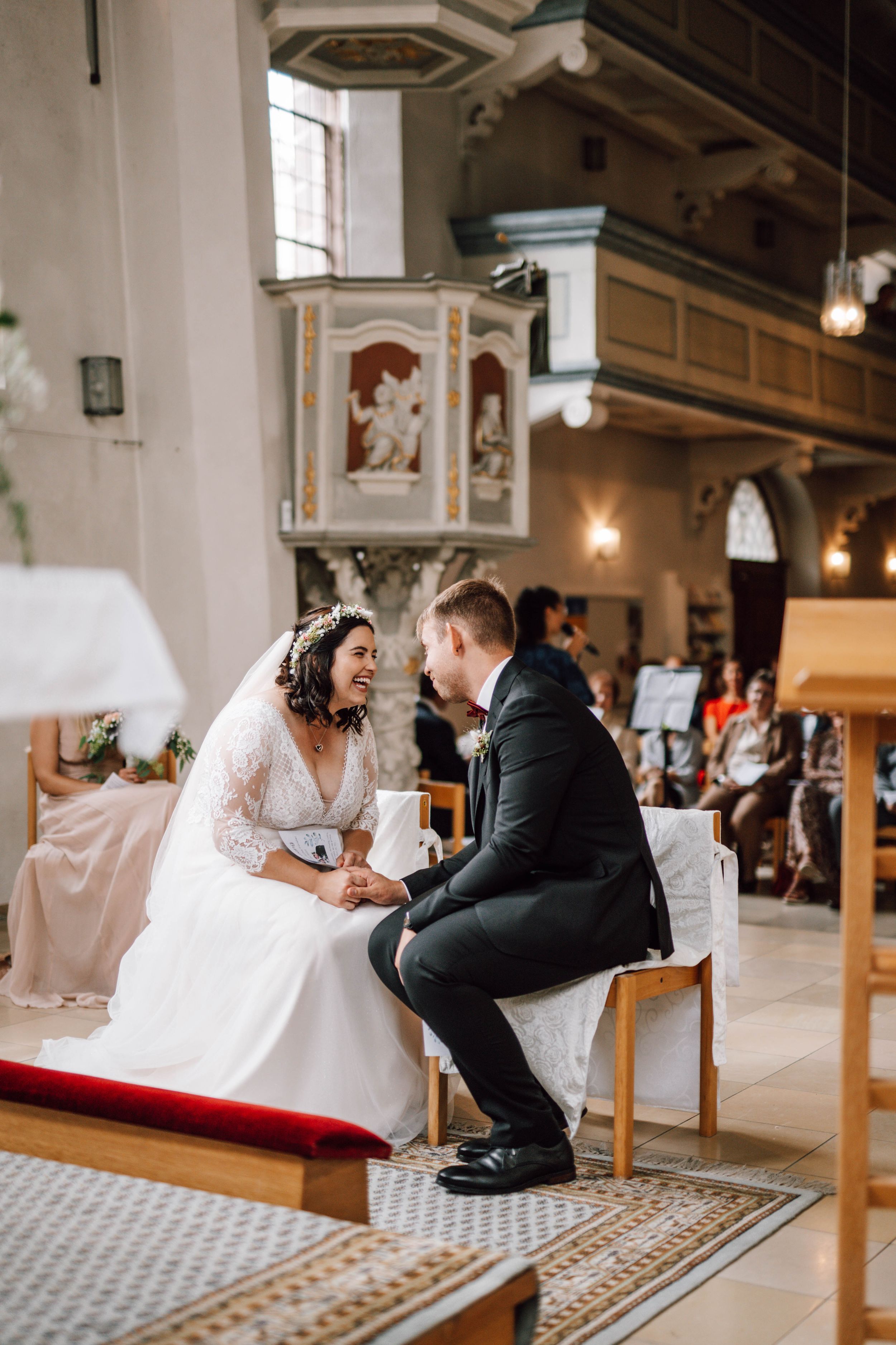 Wedding couple sits together on church pews during their ceremony.