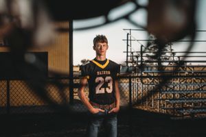 Young football player in Baldwin number 23 jersey standing by chain-link fence at sunset.