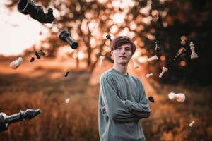 Young man with arms crossed stands confidently as chess pieces fall around him in a golden field.