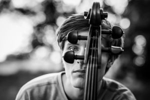 Black and white close-up portrait of a young man peering through the scroll of a cello.