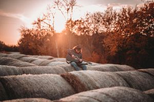 Guitarist playing acoustic guitar on hay bales during stunning autumn sunset.