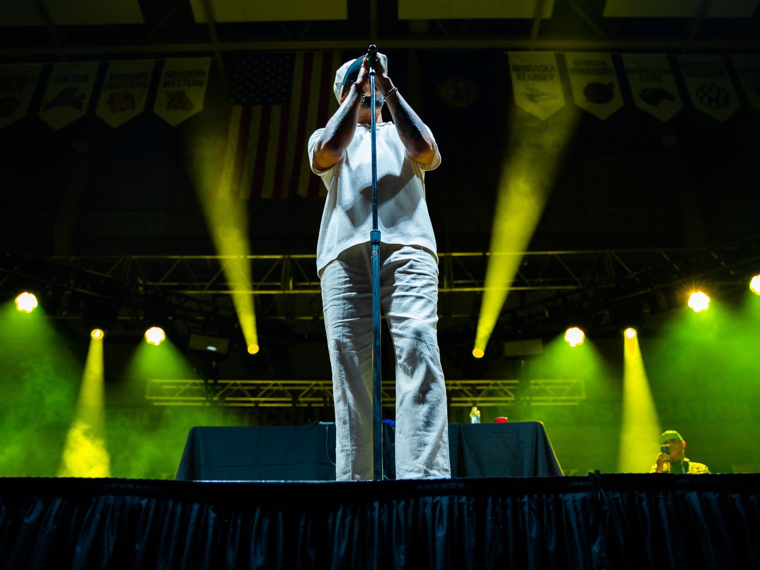 A performer stands alone on an illuminated stage with dramatic yellow spotlights during a concert.