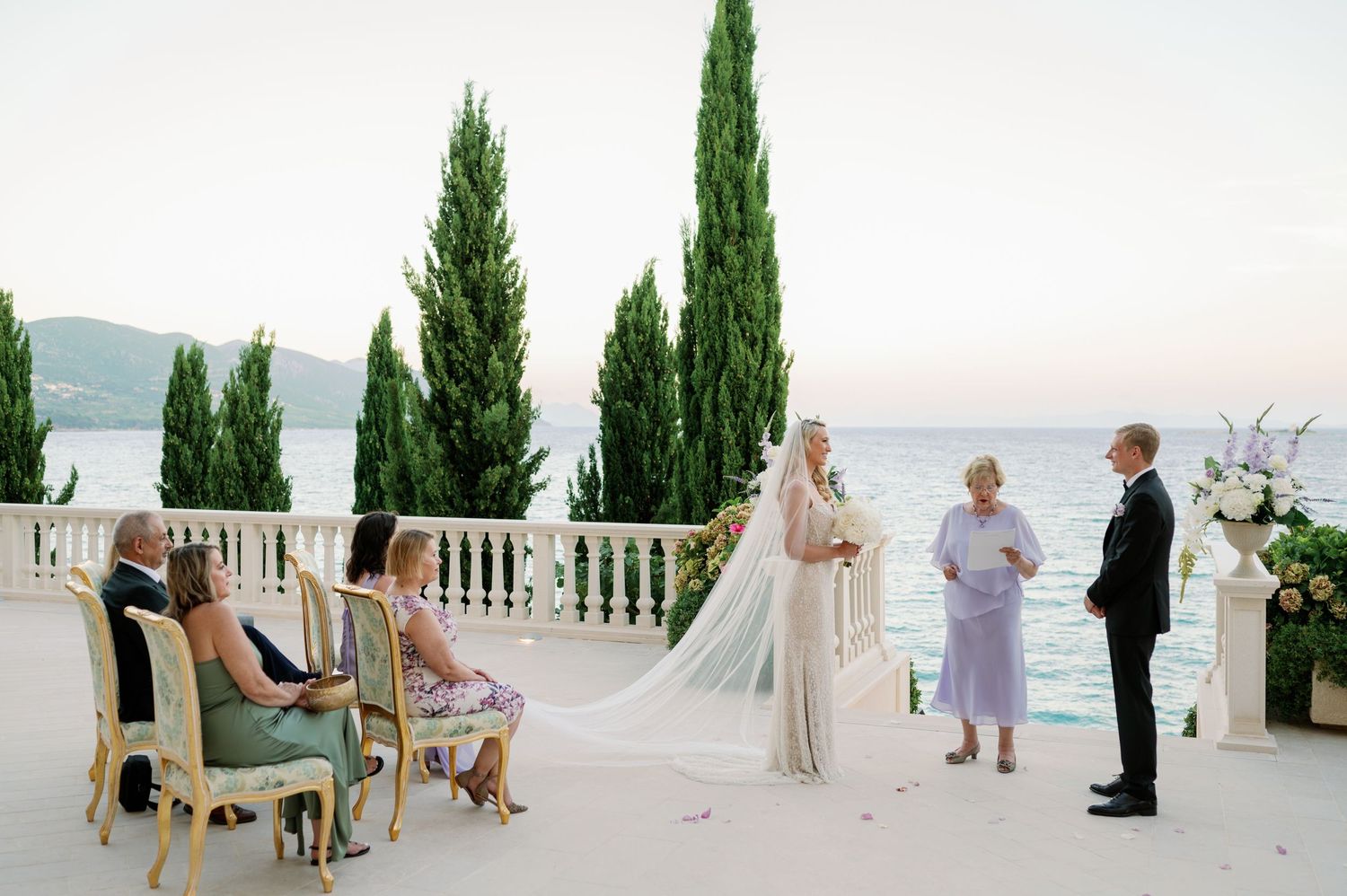 Wedding ceremony on Mediterranean terrace with cypress trees and white floral decorations.