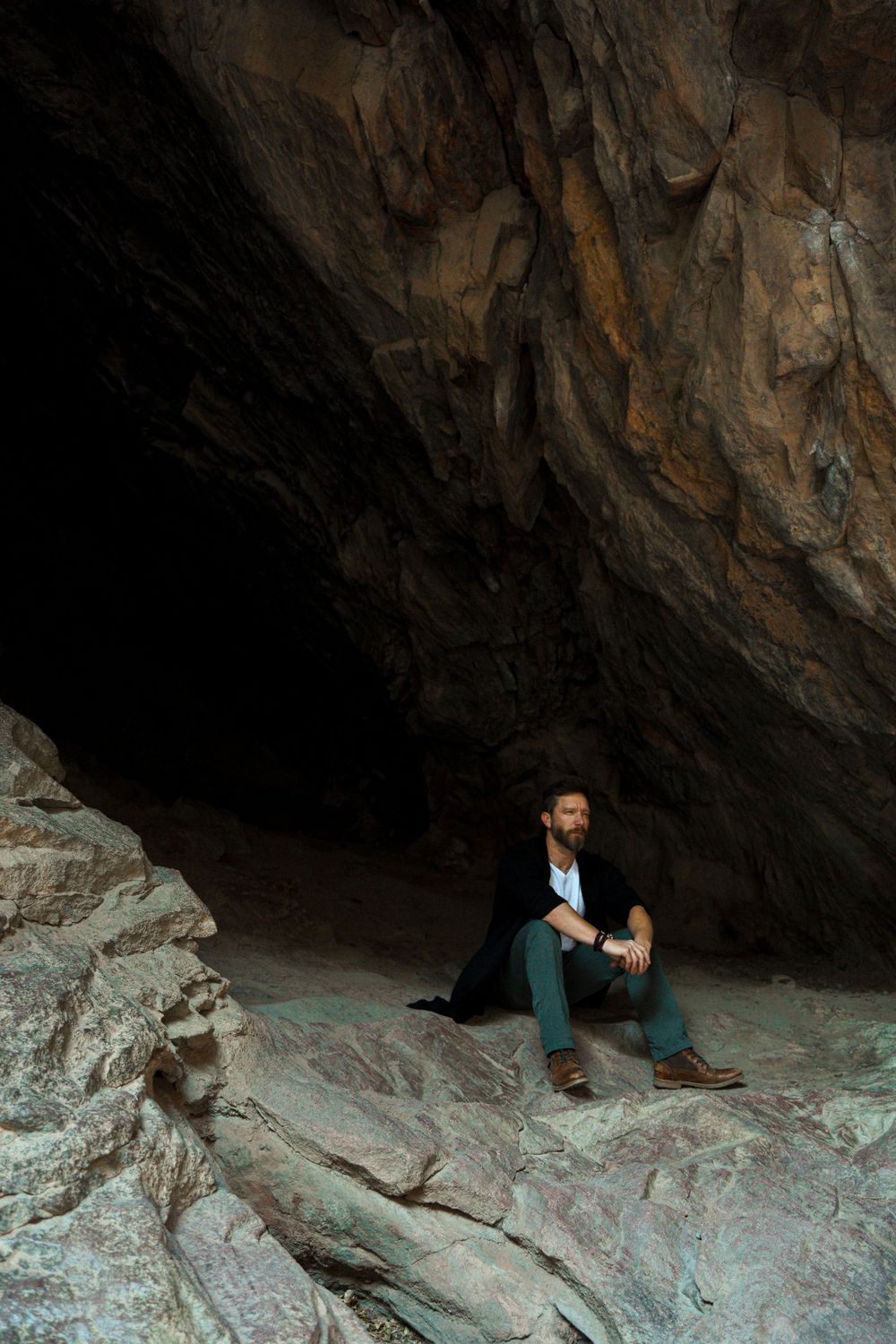 Person sitting thoughtfully in a dramatic cave setting surrounded by rocky formations.