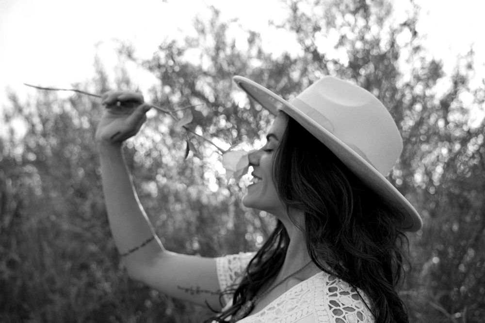 Figure in a white dress and sun hat holds a dandelion against a soft-focused natural background.