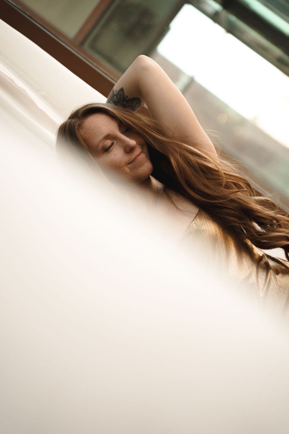 Artistic portrait of long brown hair cascading across a light colored background in soft lighting.