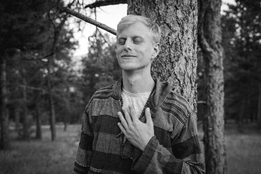 Black and white portrait of someone in a striped sweater leaning against a tree with closed eyes.