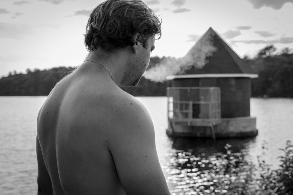 Black and white photo of a figure overlooking a lake house on the water.