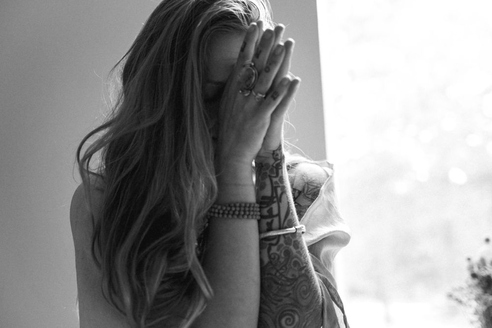 Black and white image of a person with long hair covering their face with their hands.