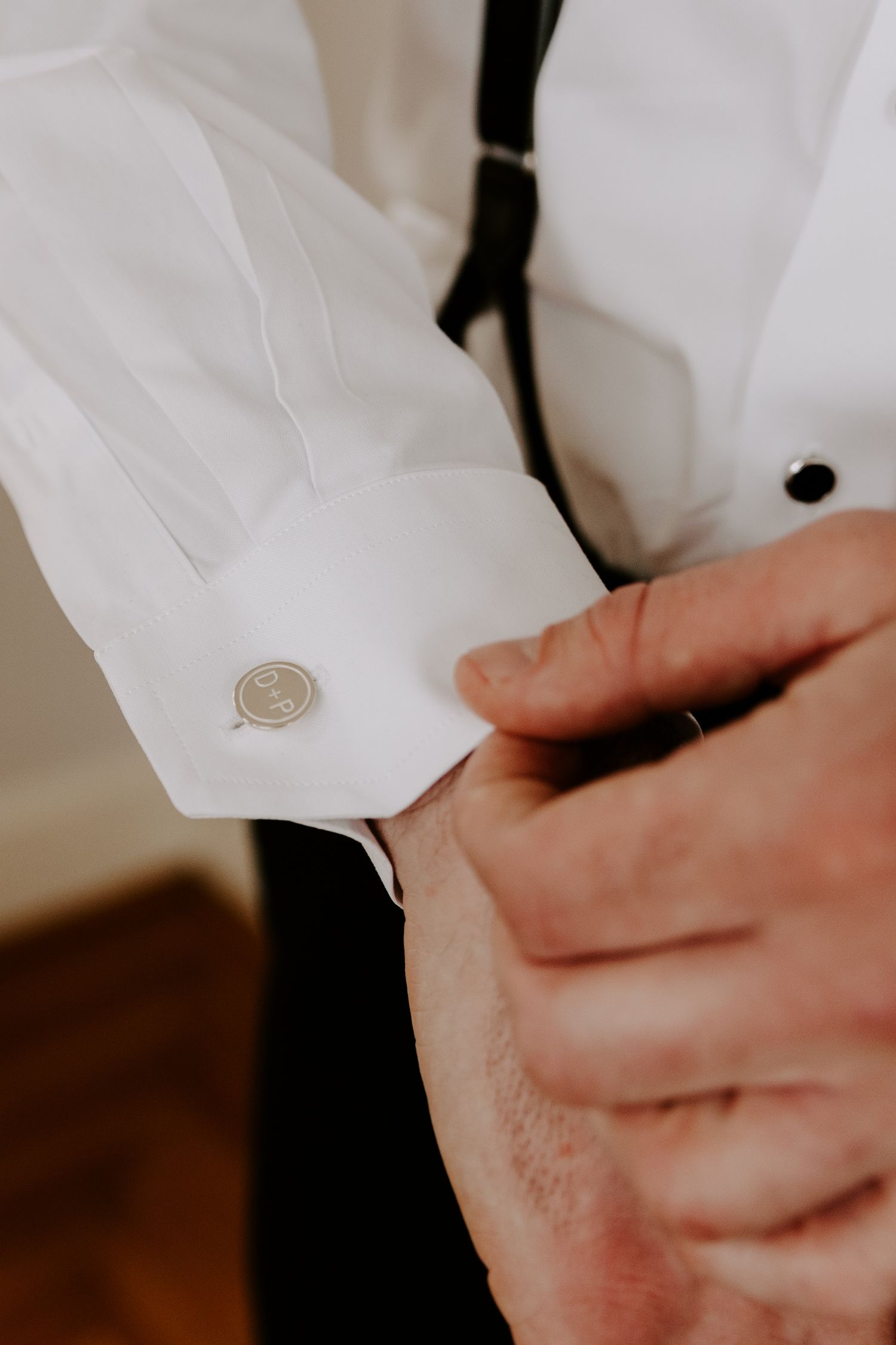 Close-up of hands adjusting a silver cufflink on a crisp white dress shirt.