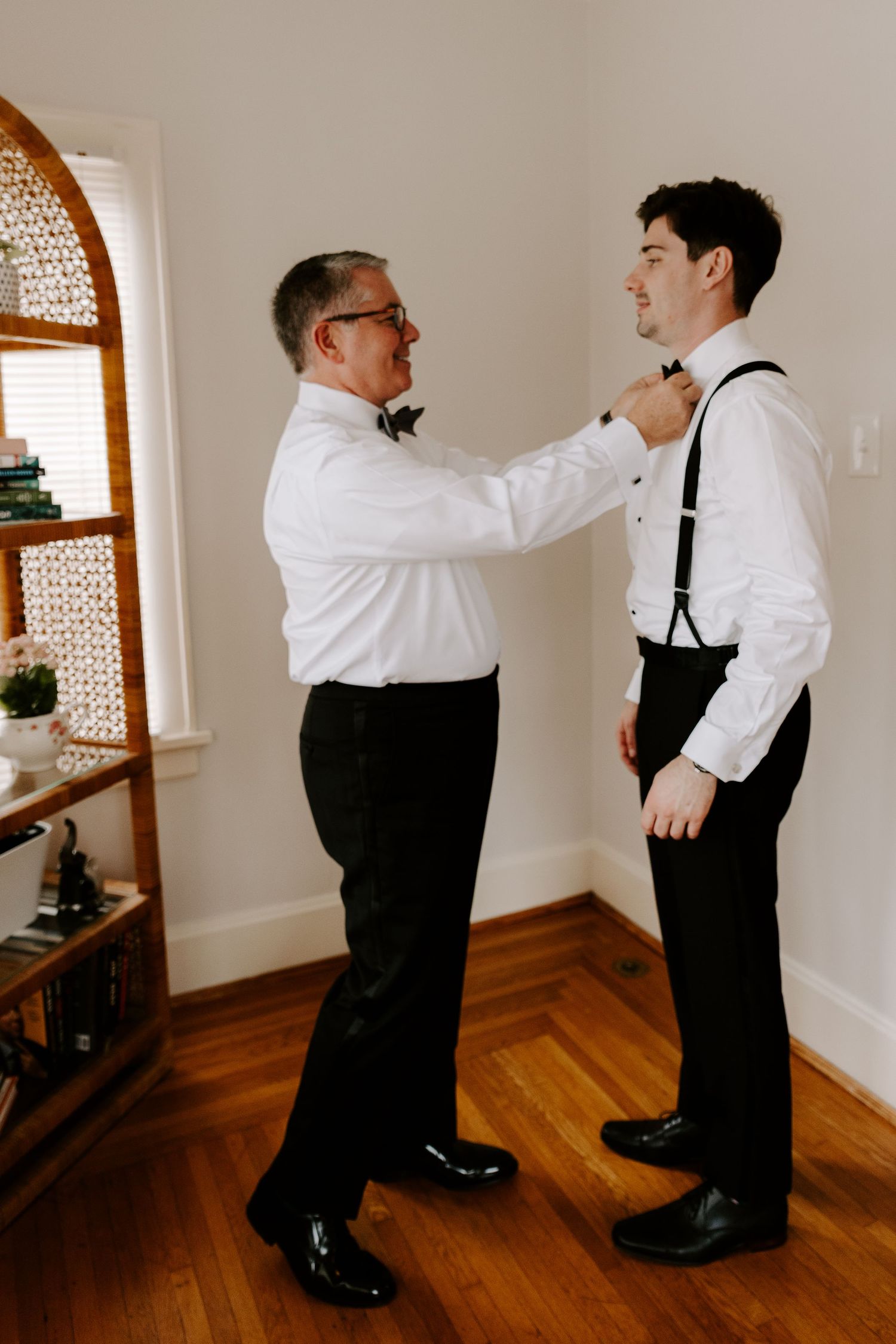 A formal pre-wedding moment showing final adjustments to attire in a sunlit room.