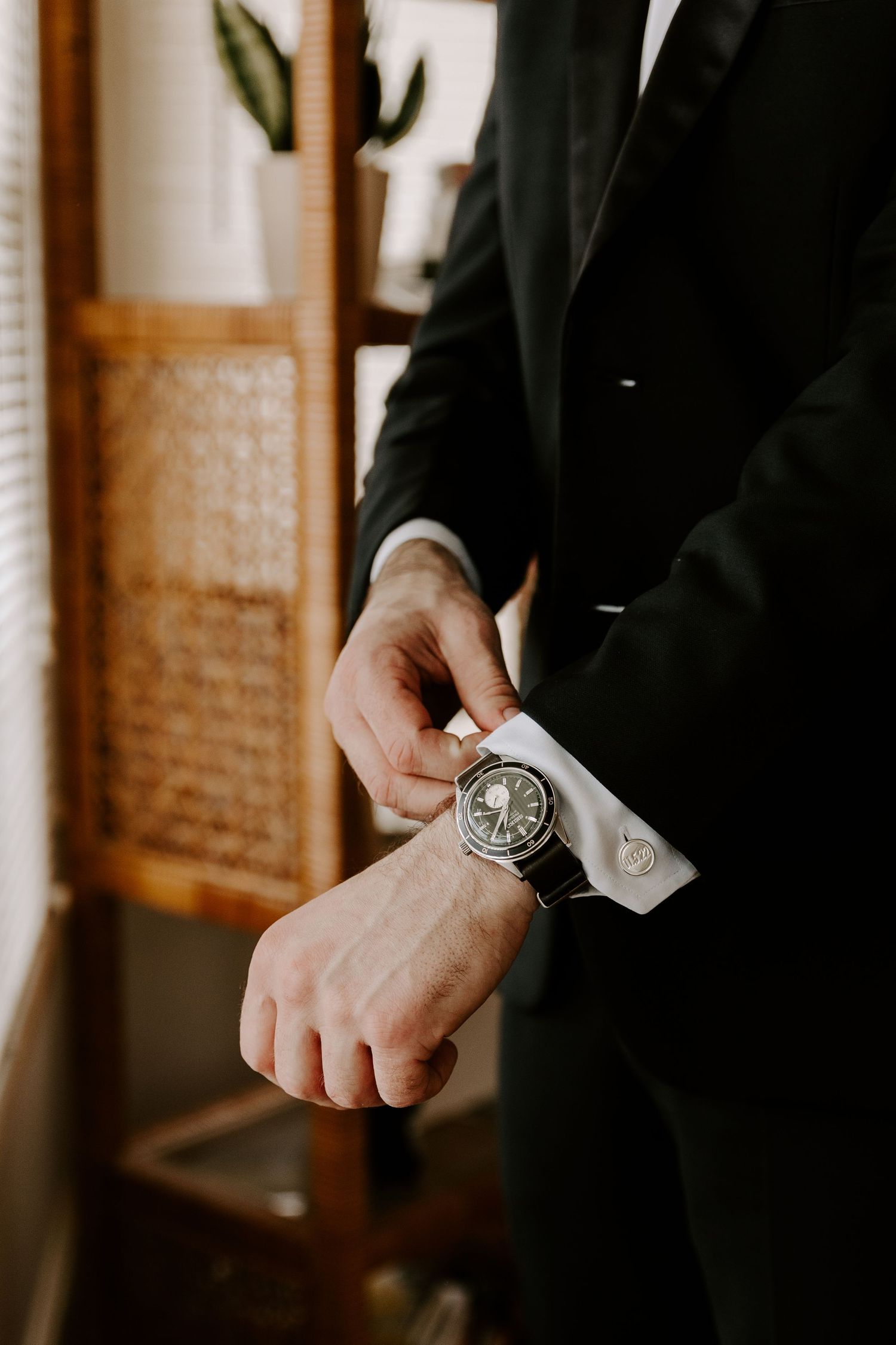 Detailed shot of a wristwatch and cufflink adjustment on a formal black tuxedo sleeve.