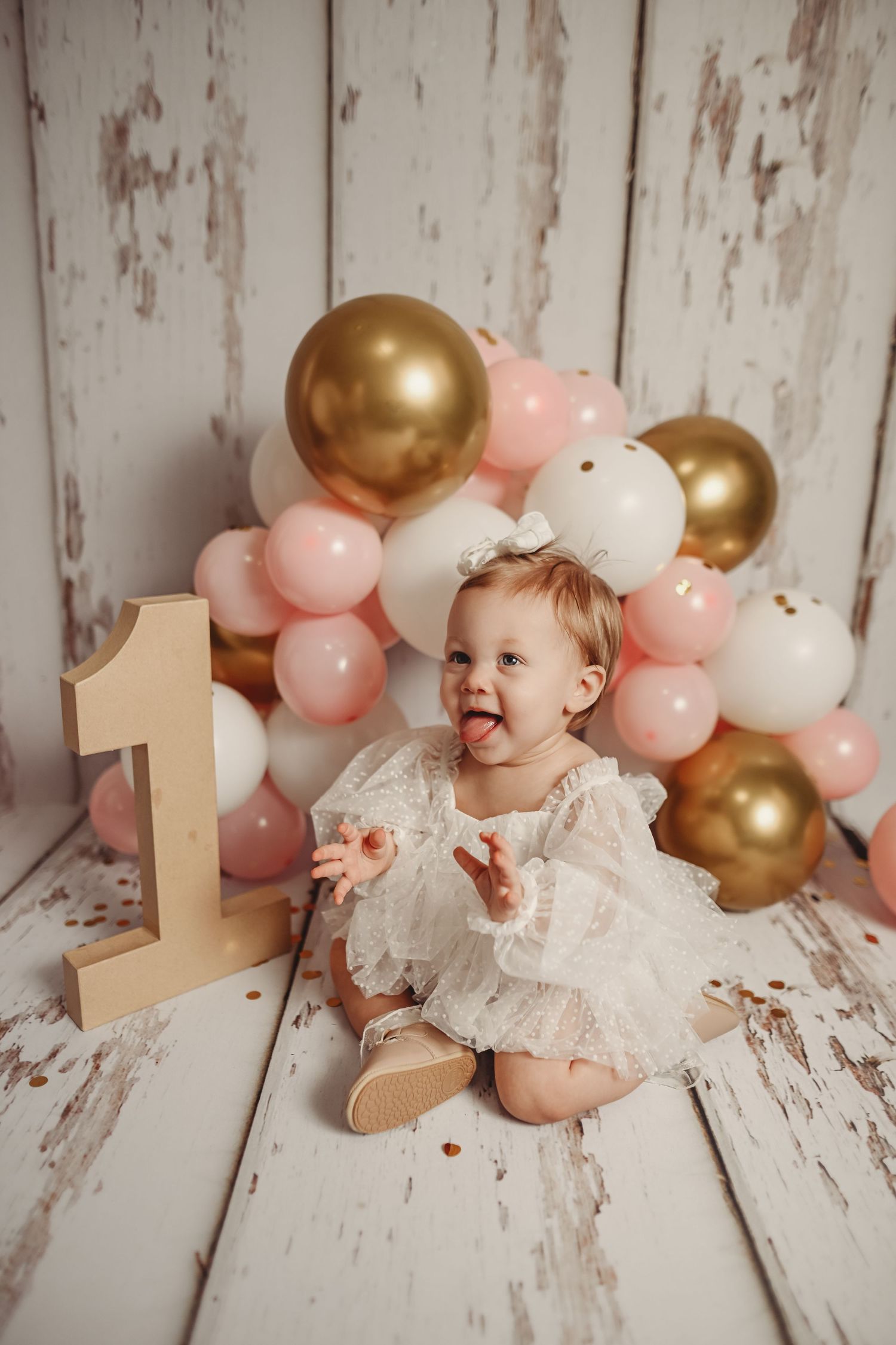 First birthday celebration with gold and pink balloons against rustic white backdrop.