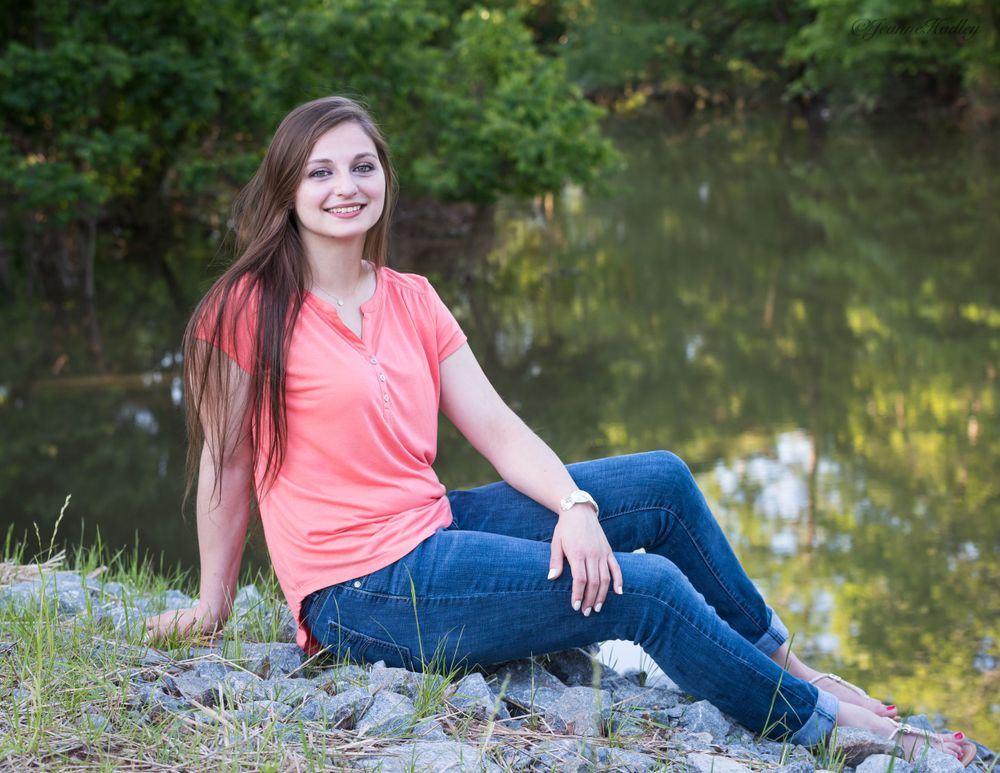 young brown haired girl in blue jeans reclining by Lake Maumelle