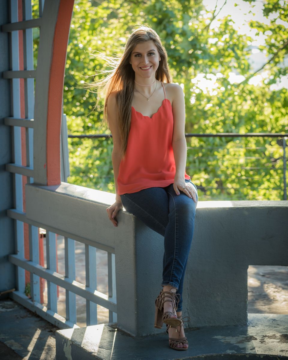 young woman with orange blouse casually sitting with legs crossed in a Pavillion summer greenery downtown Little Rock
