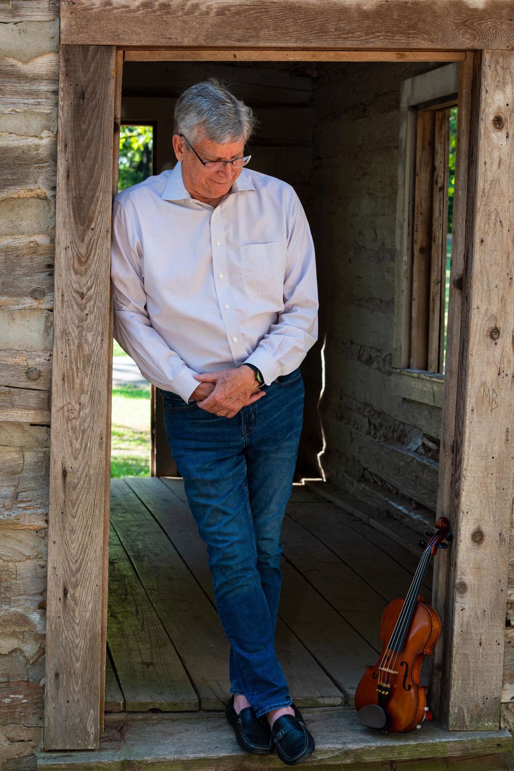 man looking down at violin in doorway of cabin in burns park north Little Rock ar senior portrait