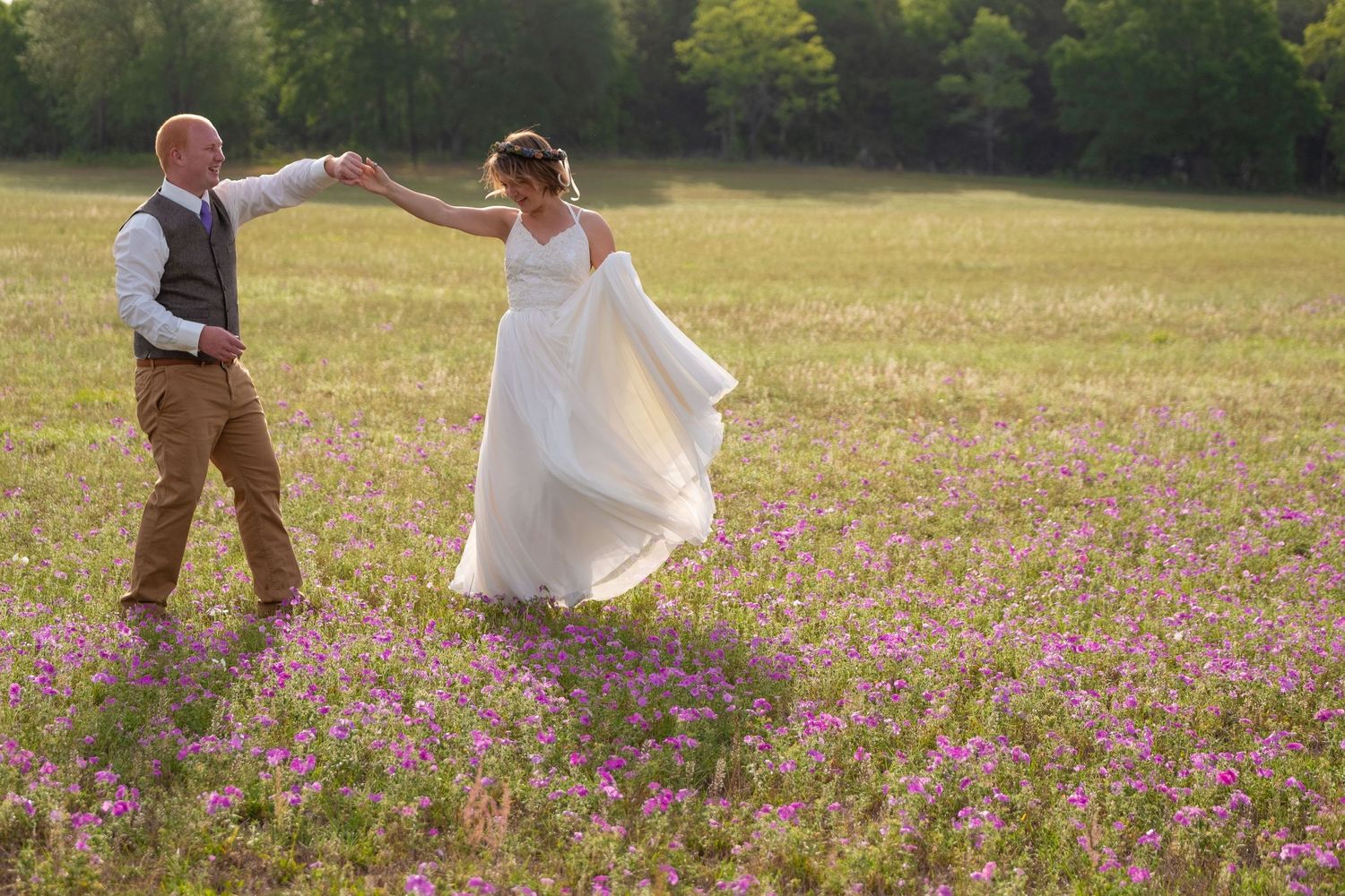 Newlyweds dance in field of purple wildflowers during golden hour.